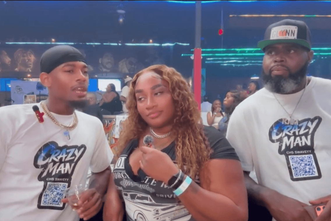 Three people standing together at an event, two men and one woman, with a crowd and bright lights in the background.
