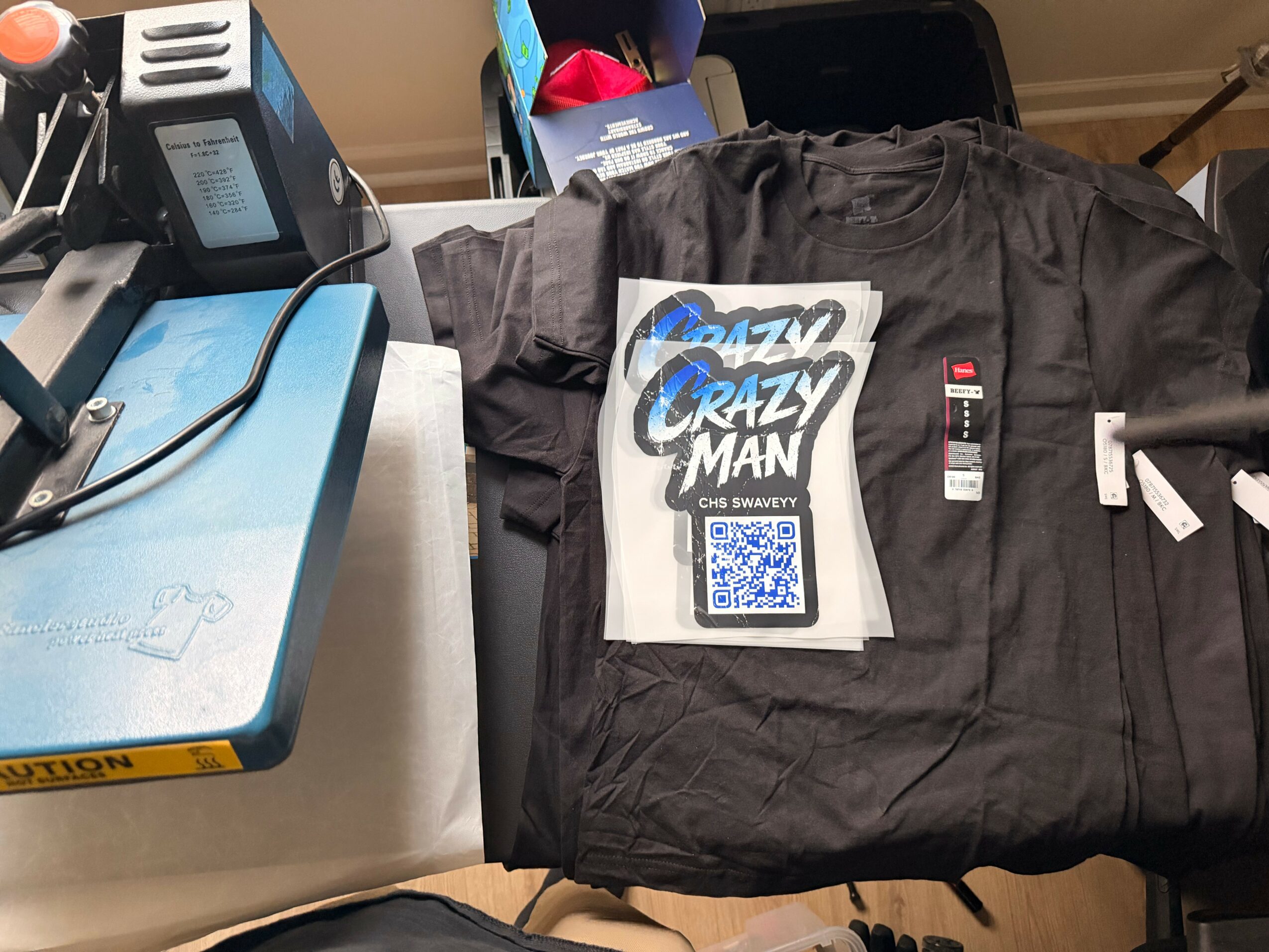 Black jacket with tags and a QR code, placed on a cluttered desk with various objects around.