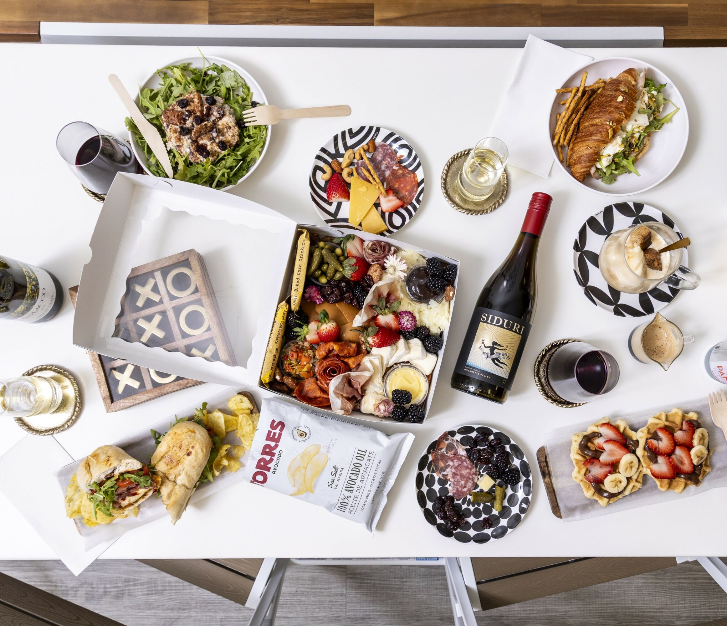 Table with salads, a bottle of wine, desserts, and various dishes, viewed from above.