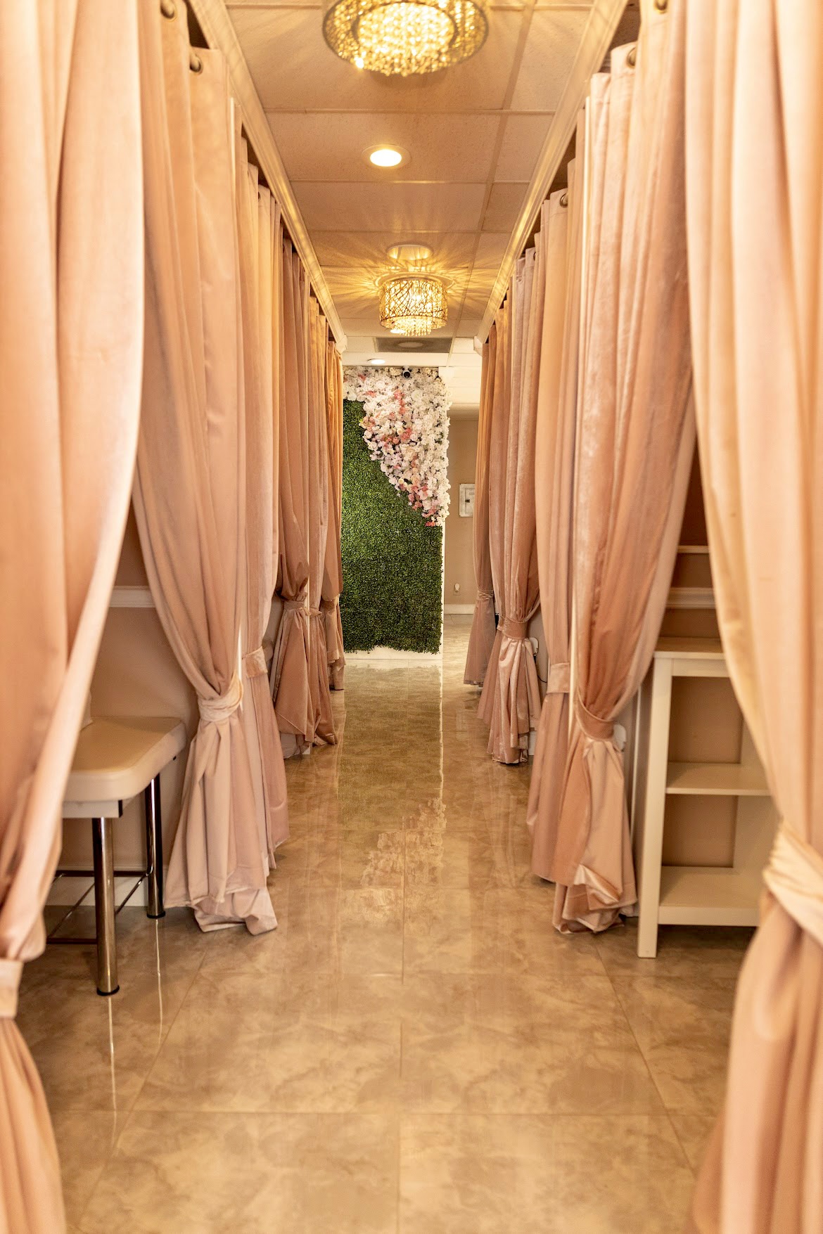 Narrow corridor with pink curtains on both sides, leading to a floral backdrop at the end, with chairs and a small table visible.