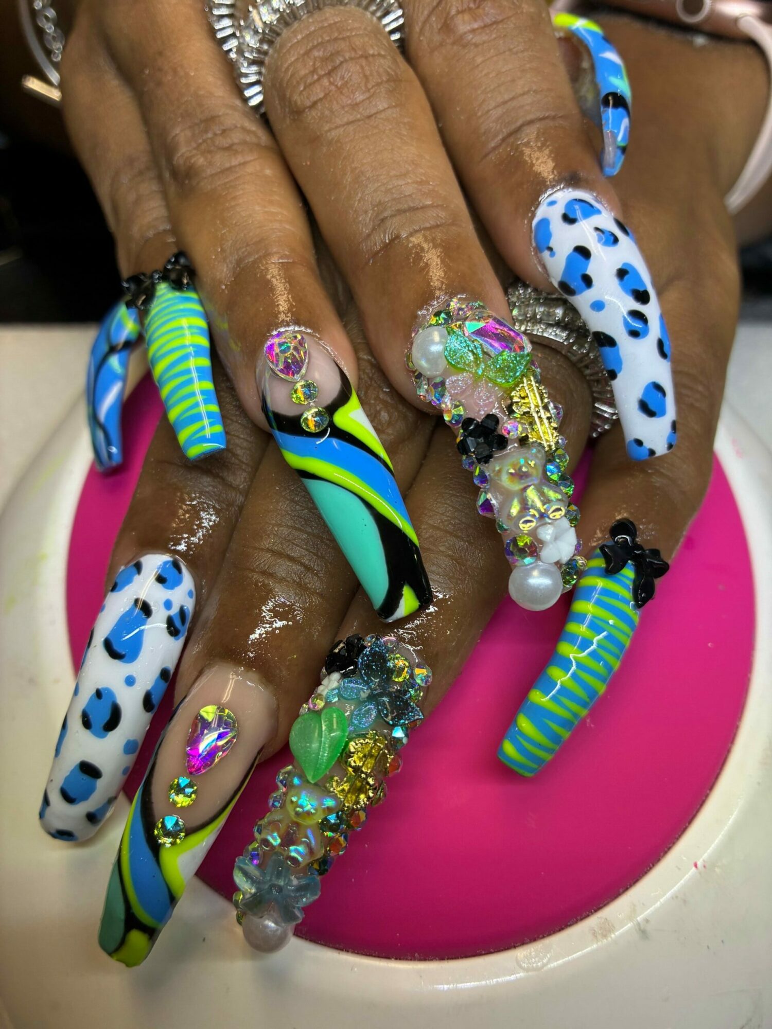 Close-up of hands with decorated, colorful, and patterned artificial nails resting on a pink surface.