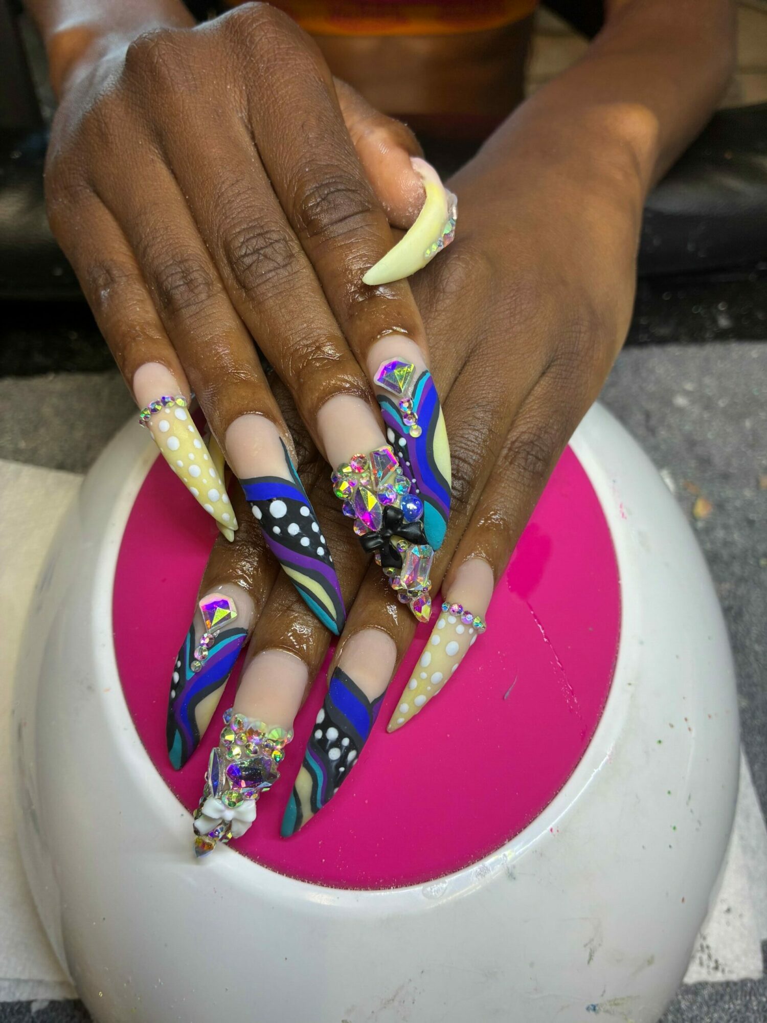 Person's hands with decorated nails being dipped into a pink liquid in a white bowl.
