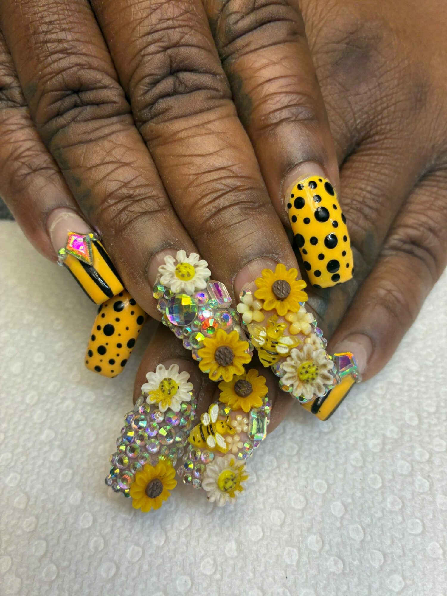 Close-up of hands with decorated nails and small yellow and white flower embellishments, on a white textured background.