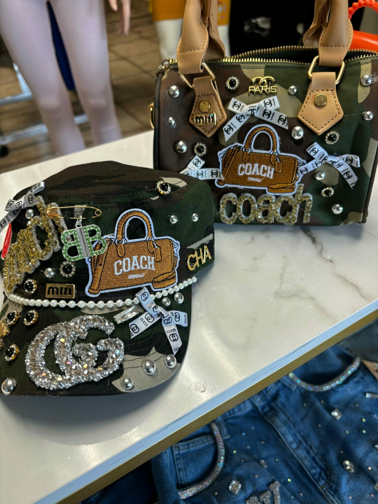 Two decorated handbags with lock and chain embellishments on a table, with a person in jeans in the background.