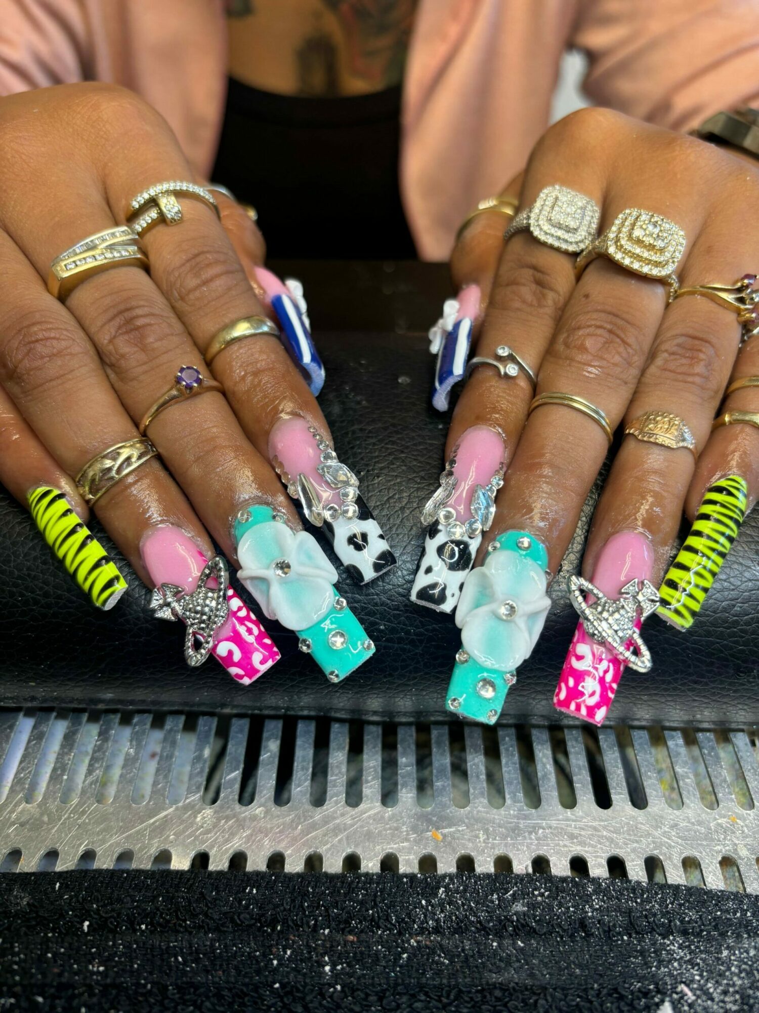 Close-up of hands with decorated nails and gold rings, resting on a black textured surface.