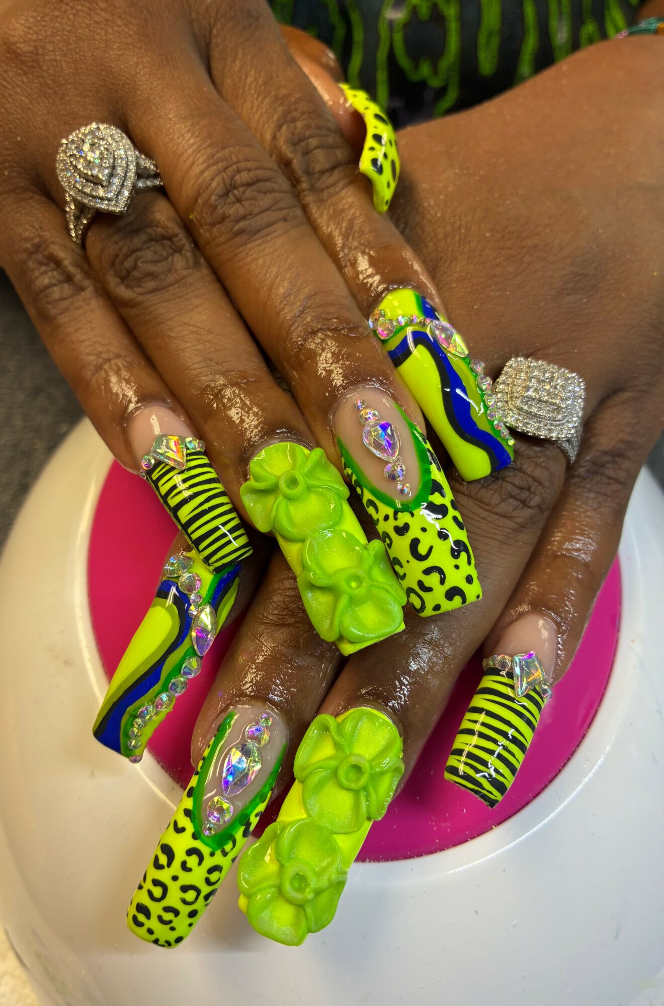 Hands with colorful, decorated nails and rings resting on a pink and white surface.