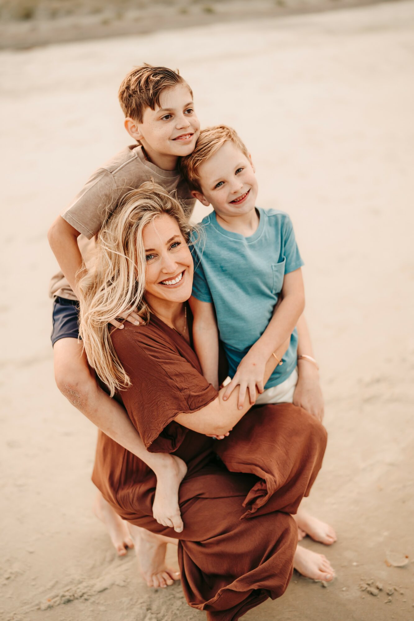 Woman with two children on a sandy beach, all smiling and looking at the camera.