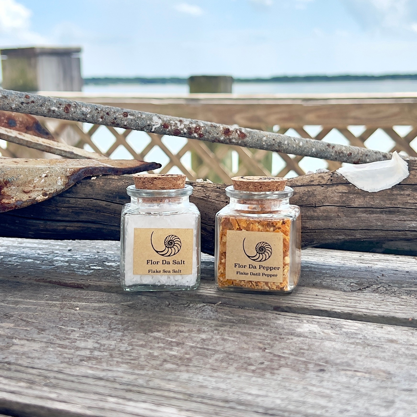 Two small glass jars with labels, one containing salt and the other pepper, on a weathered wooden surface outdoors.