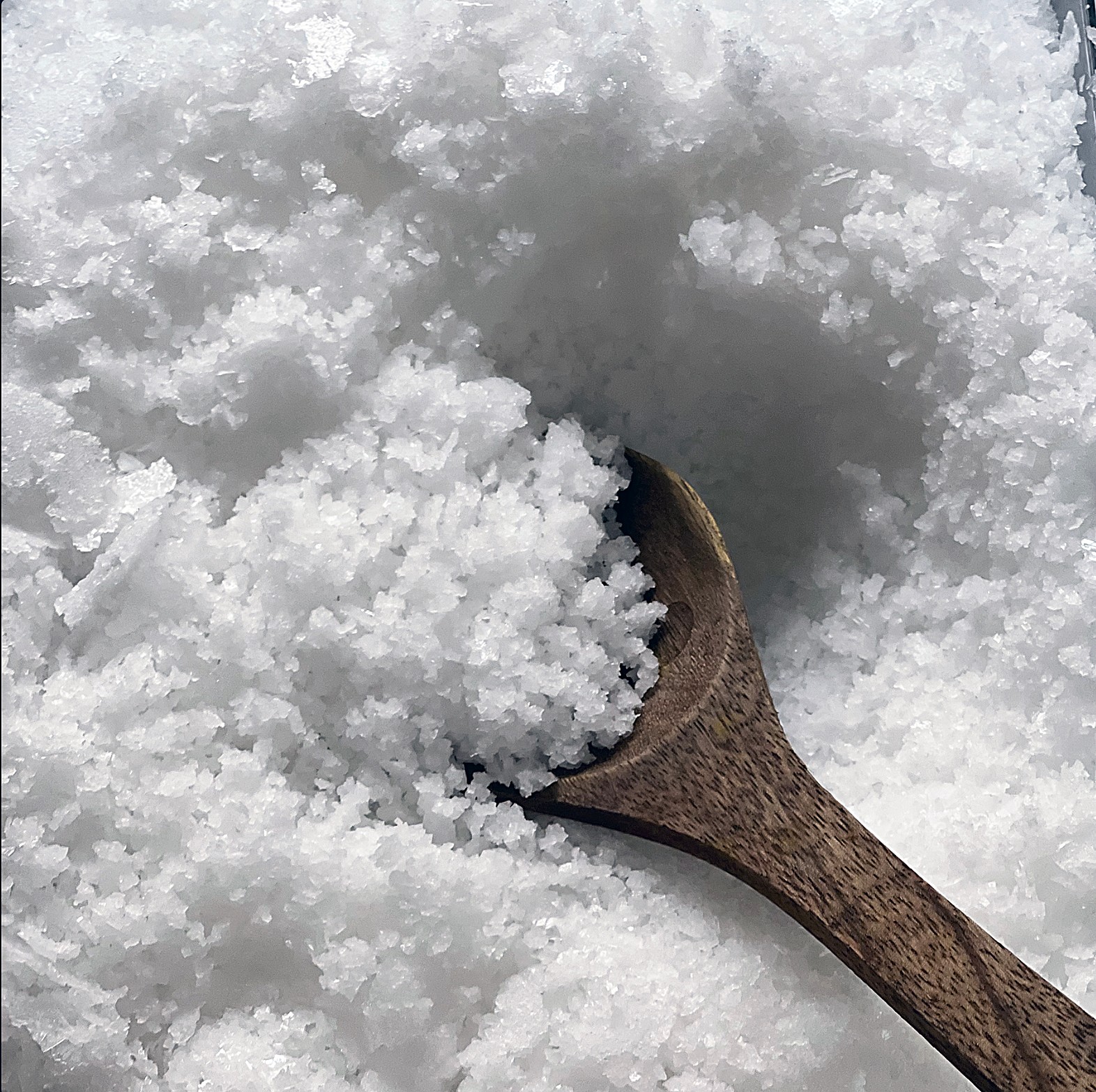 Wooden spoon partially buried in snow, surrounded by snowflakes and ice crystals.