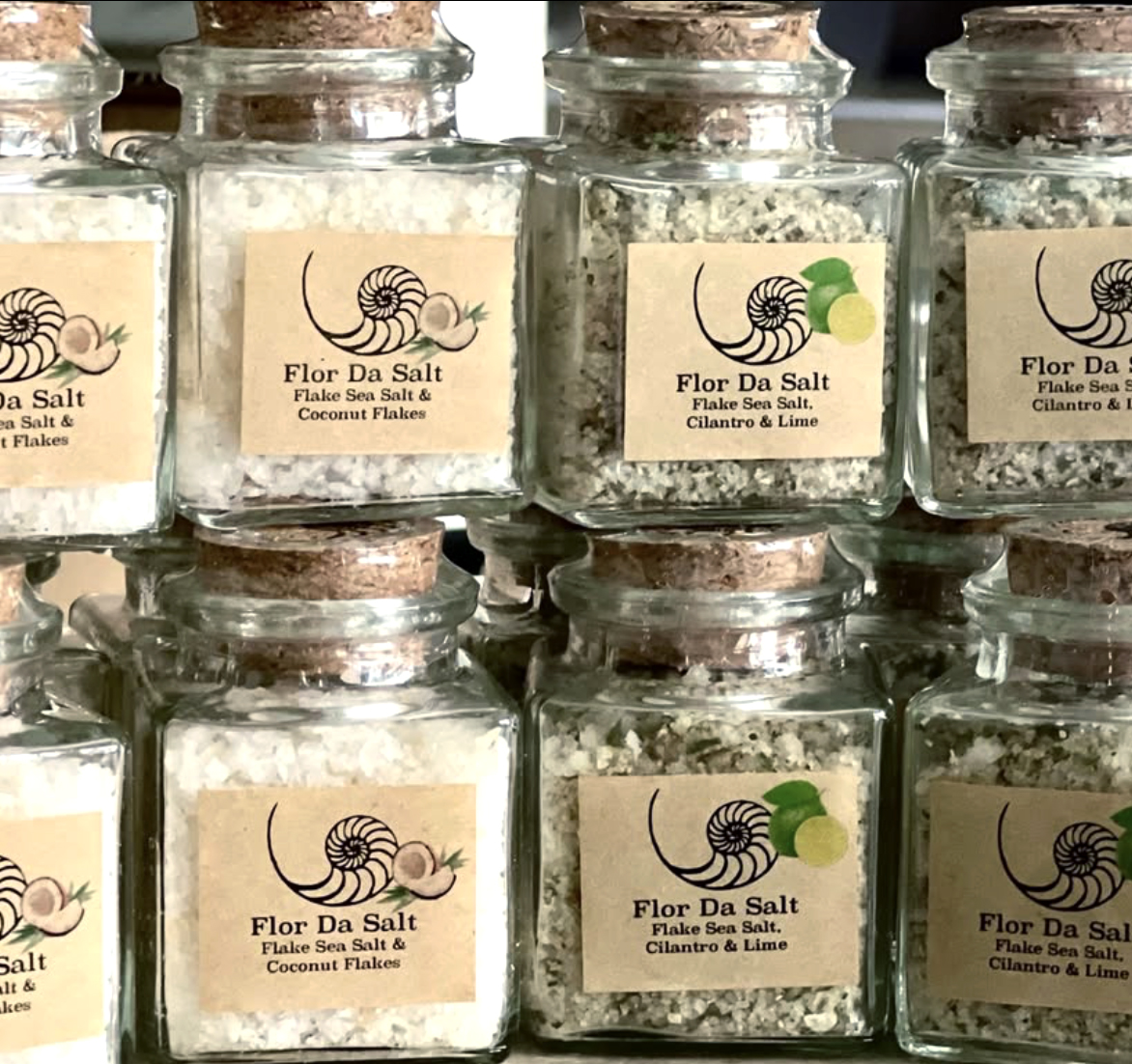 Multiple glass jars with salt, labeled with a snail logo and flavor descriptions, arranged on a shelf.