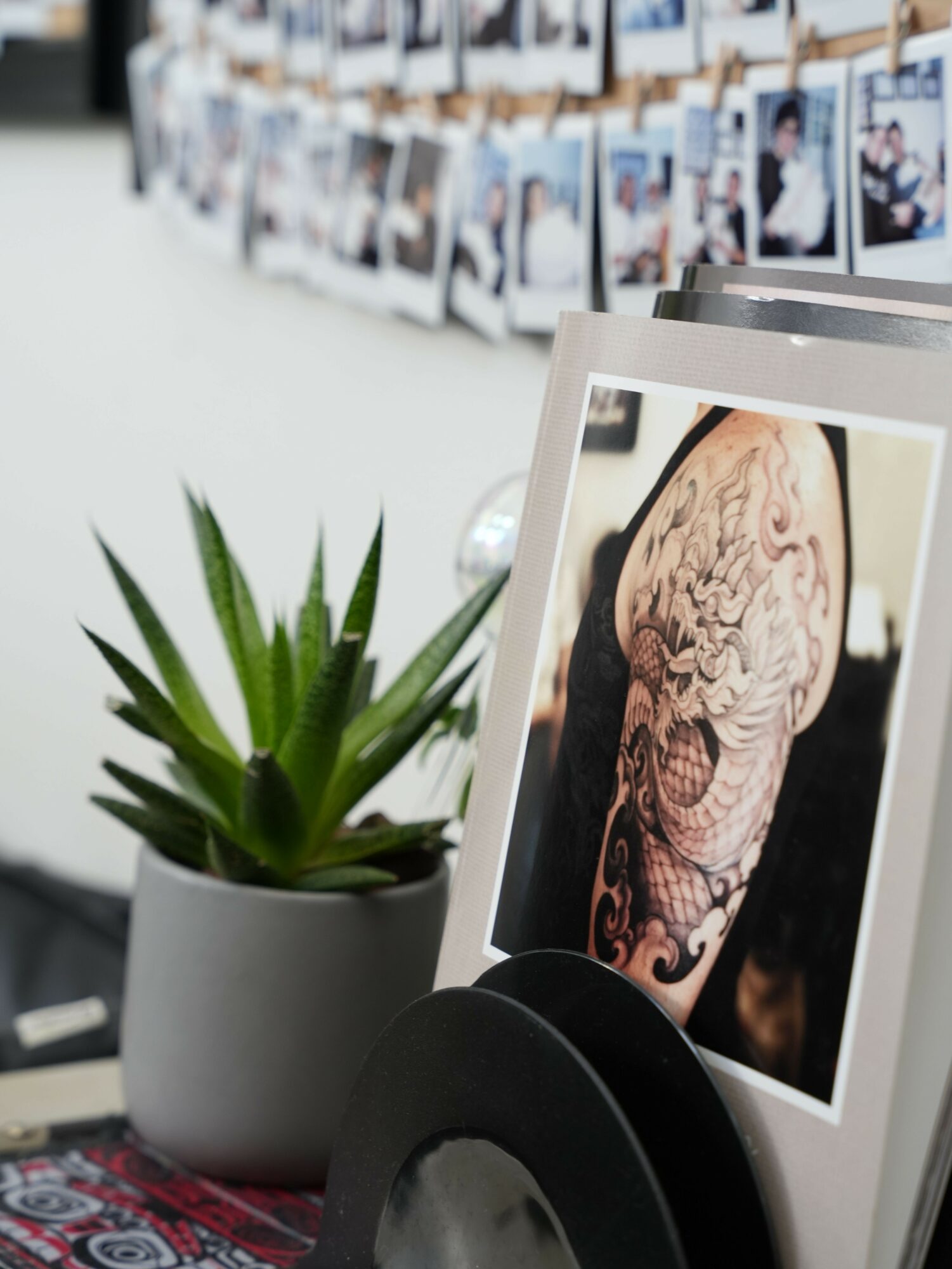 Photograph of a tattooed person's face on a printed photo, with a black hat and a potted plant nearby.