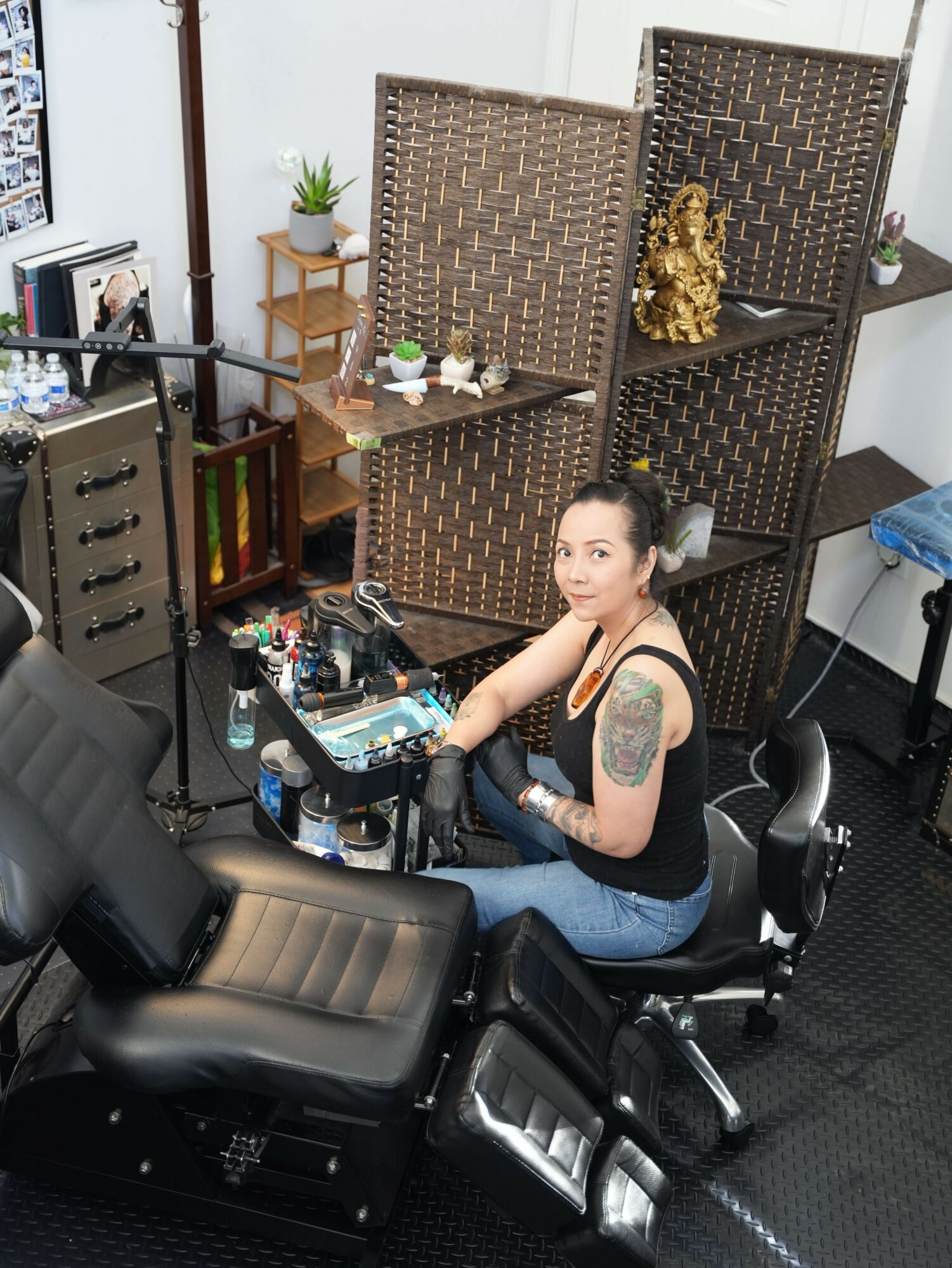 Woman with braided hair and tattoo on arm sitting at a desk in a room with furniture and decorative items.