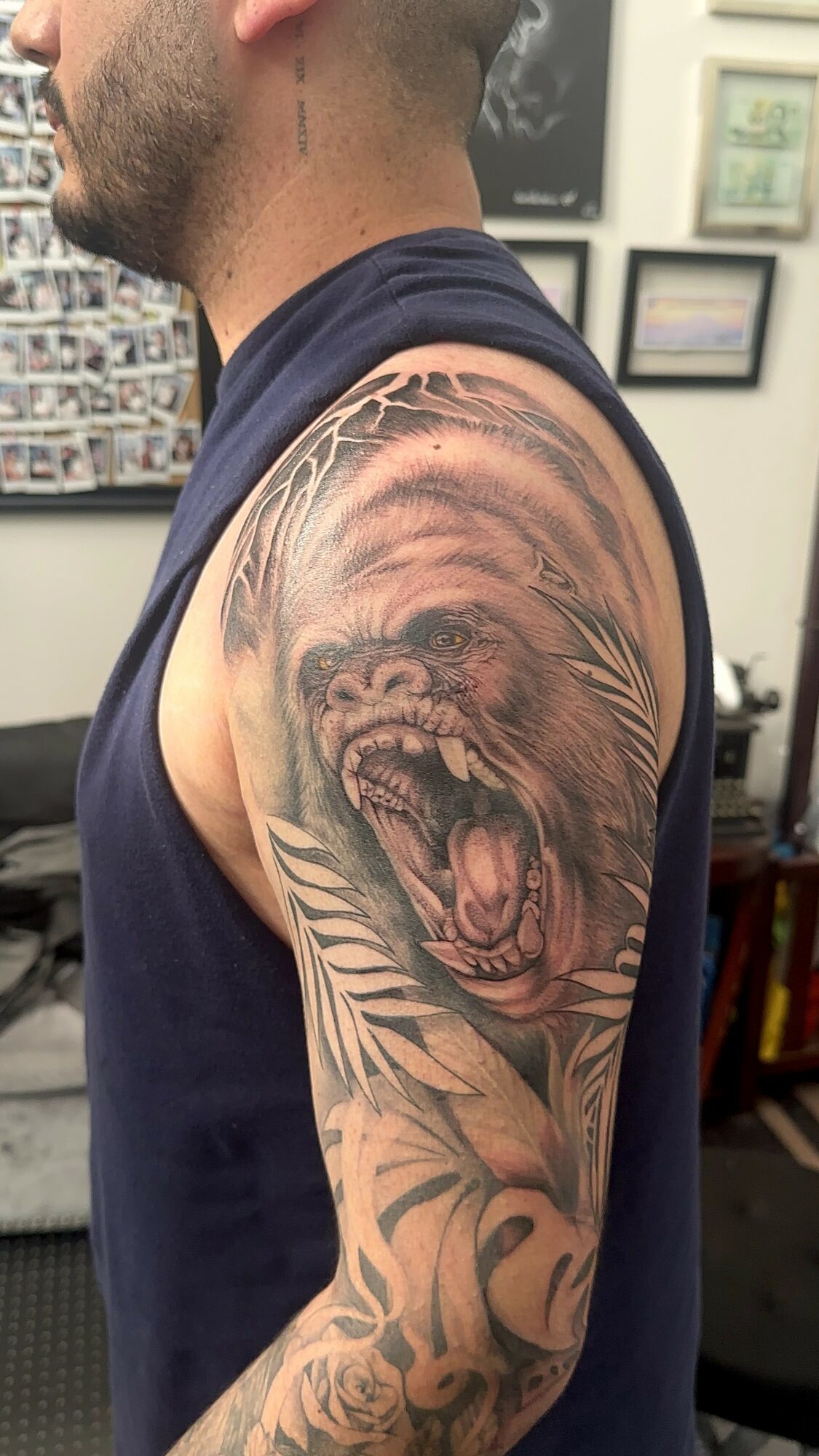Tattoo of a roaring lion's face on a person's upper arm with detailed shading and leaves background.