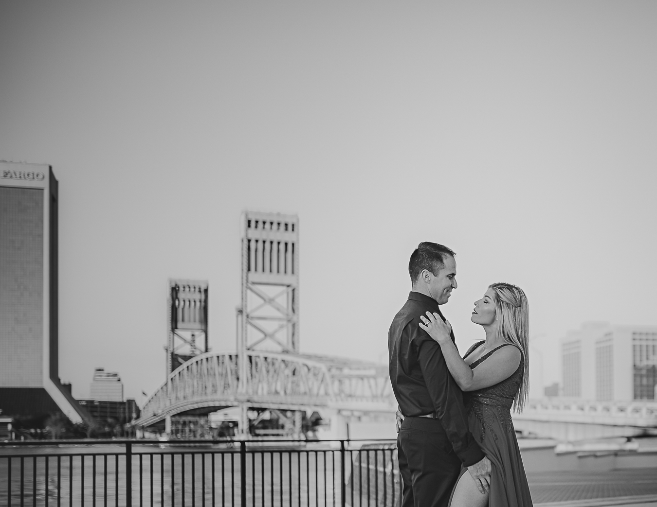 Two people standing close, facing each other, on a balcony with city buildings in the background.