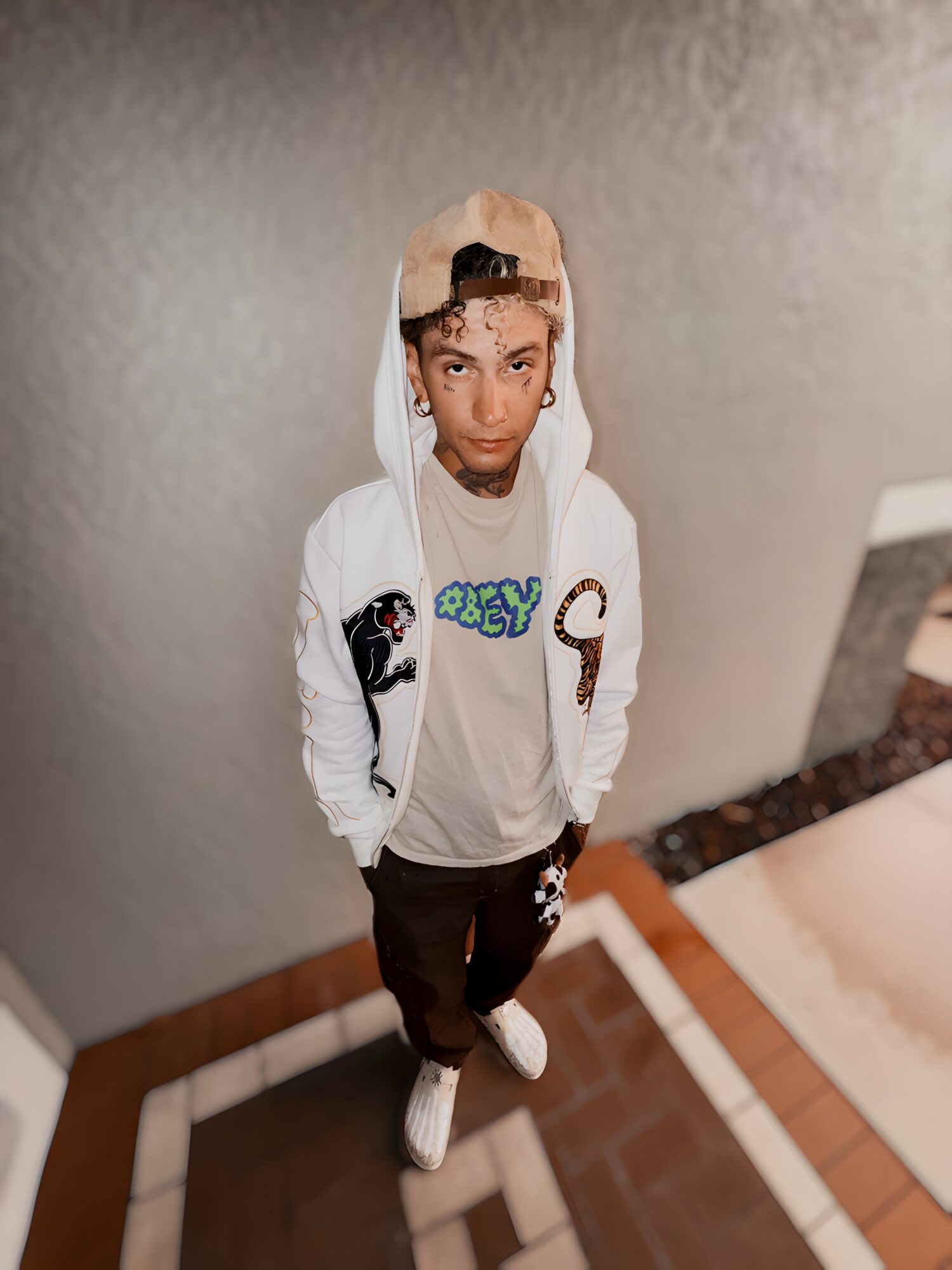 Young boy with a hoodie, standing indoors on a tiled floor, looking at the camera with hands in pockets.