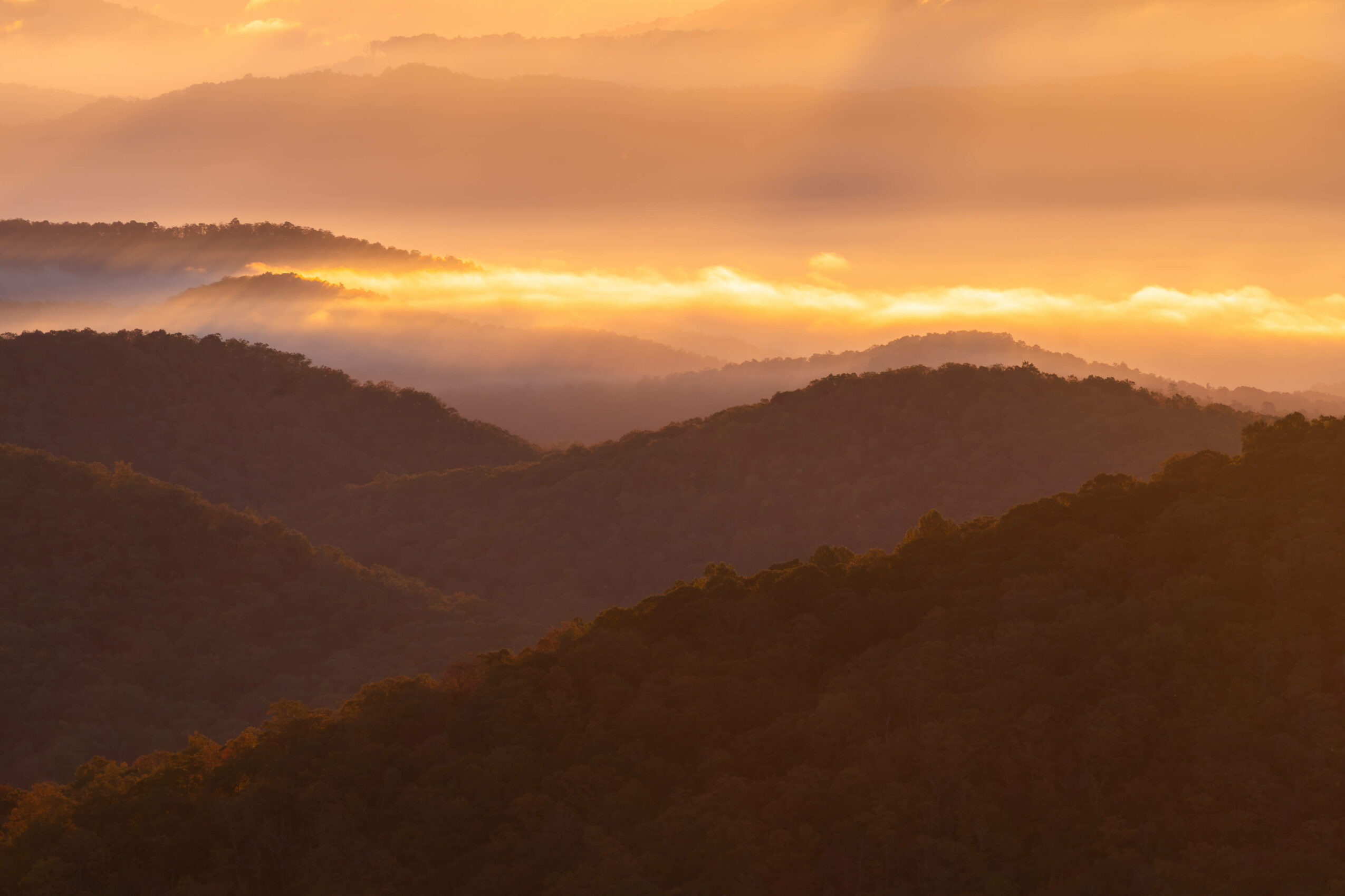 Sunset over mountain ranges with clouds and warm sky, landscape with layered hills, peaceful scene