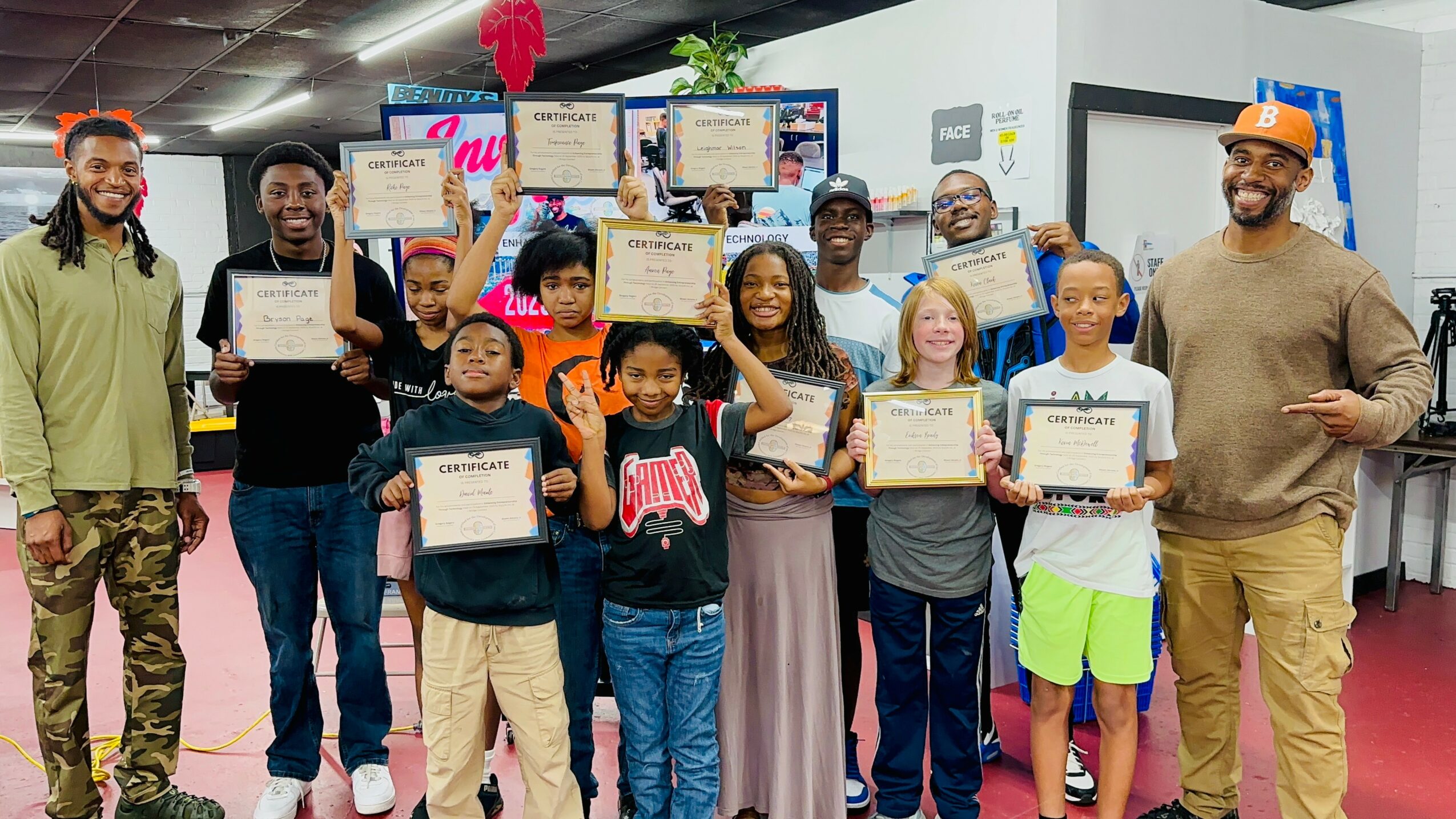 Group of children and adults holding certificates, smiling indoors with a pink carpet and decorations.