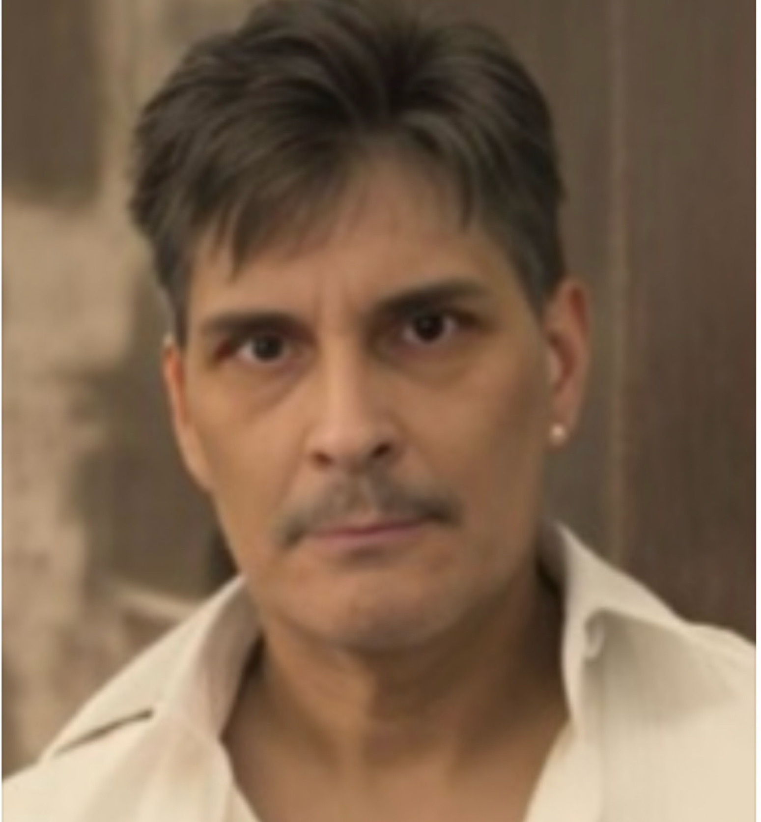 Man with short dark hair and a serious expression, wearing a light-colored shirt, in an indoor setting.