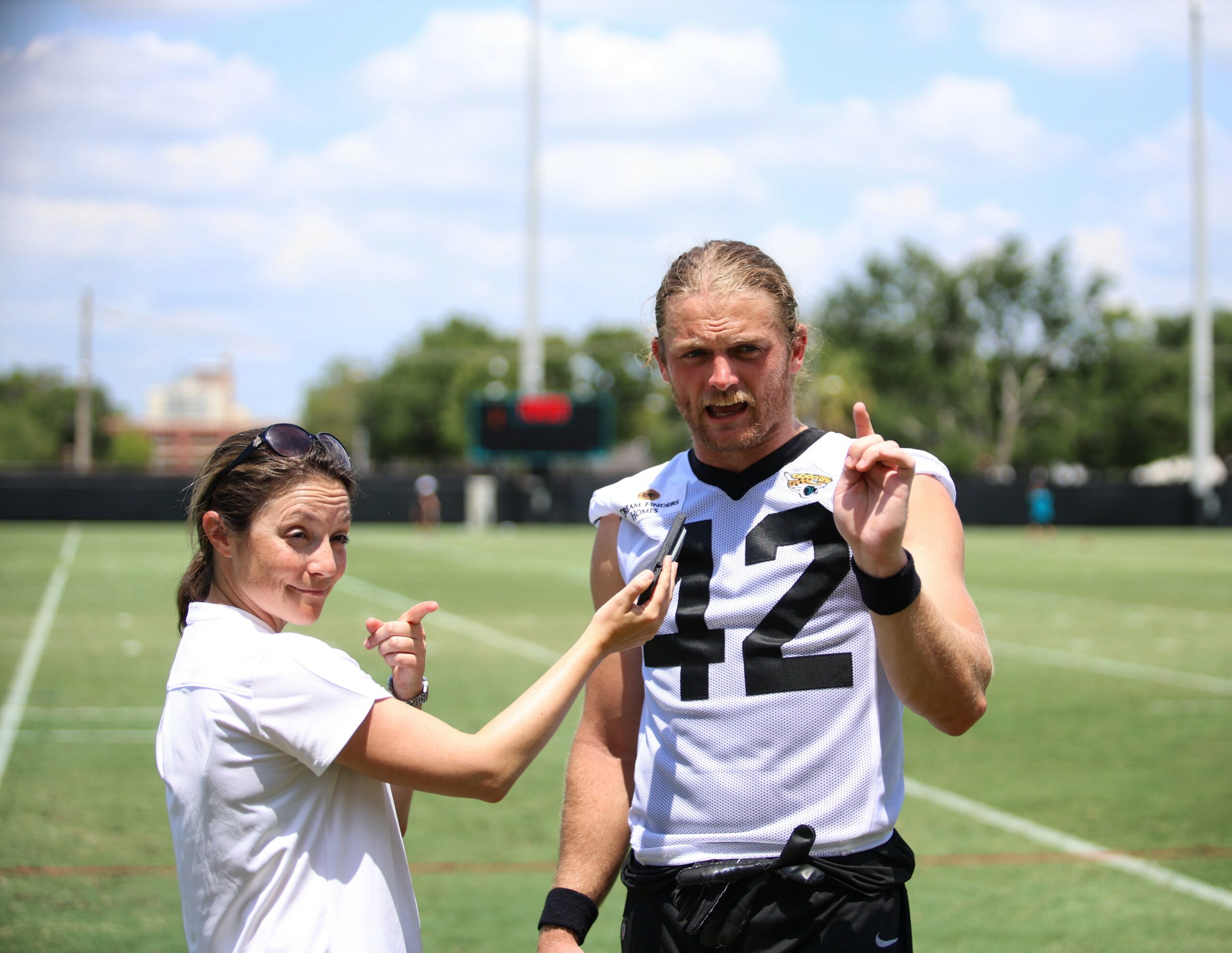 Two people on a football field, one in a jersey with number 42, the other in a white shirt, holding a phone.