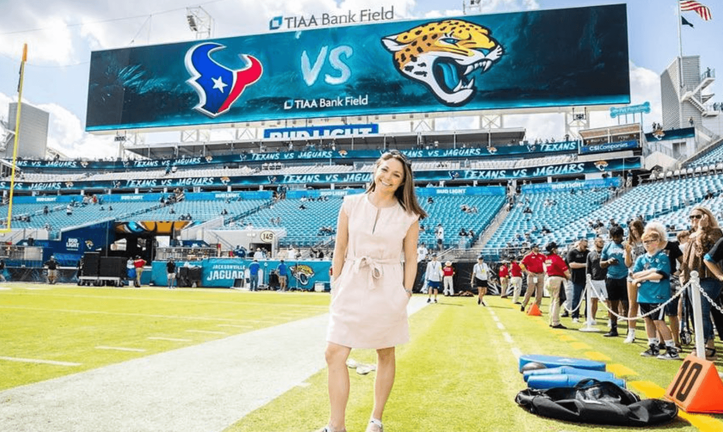 Woman standing on football field with large scoreboard showing Houston Texans and Jacksonville Jaguars logos in the background.