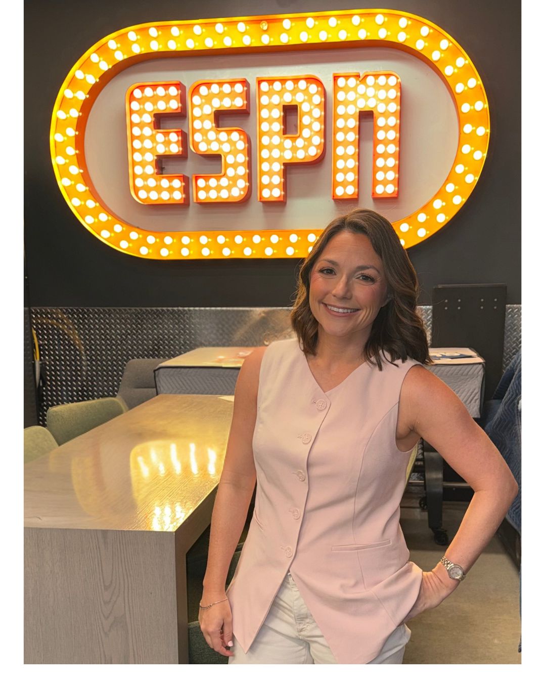 Woman smiling in front of a large illuminated ESPN sign, standing indoors with tables and chairs nearby.