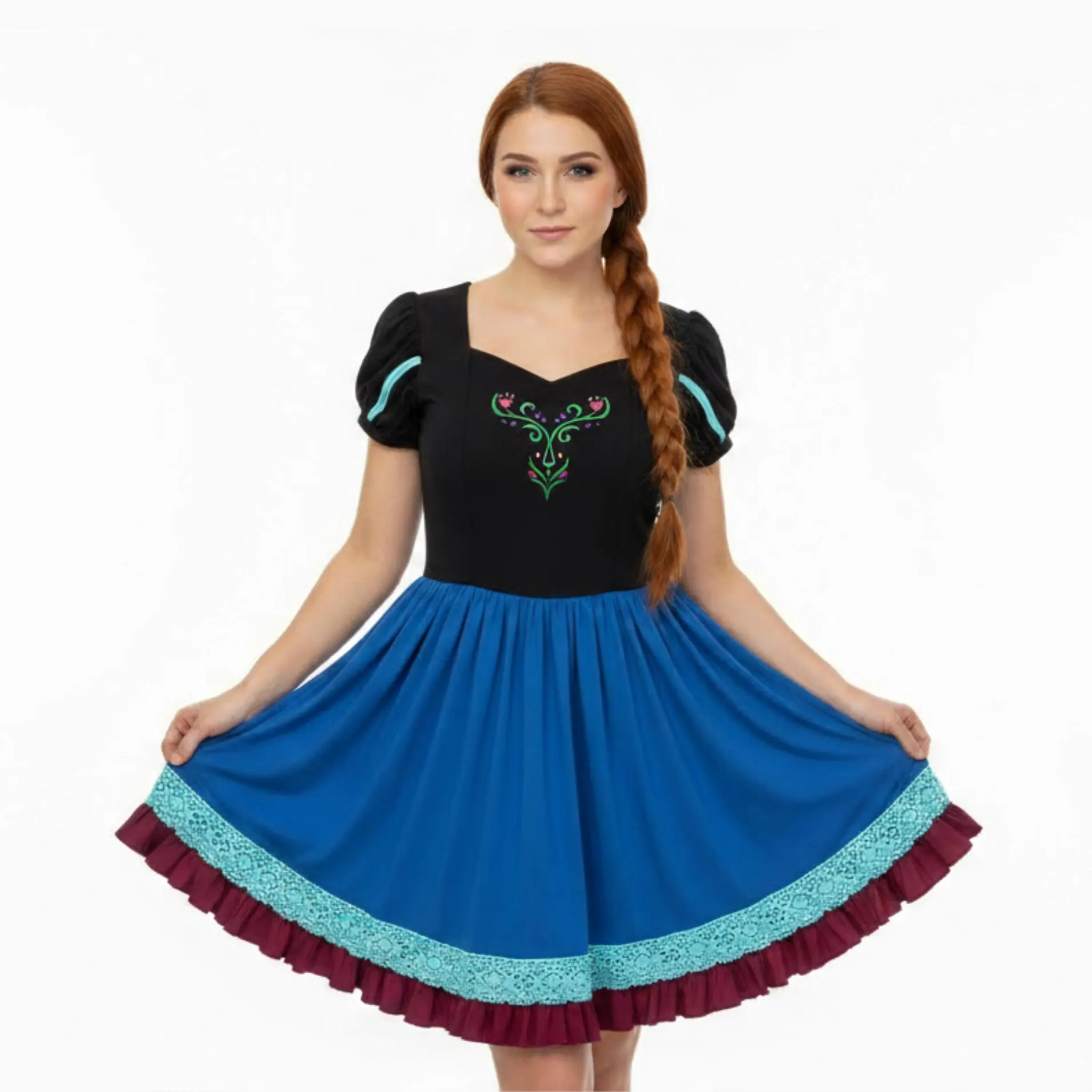 Young woman with long braided hair wearing a black and blue dress, holding the skirt outwards, standing against a white background.