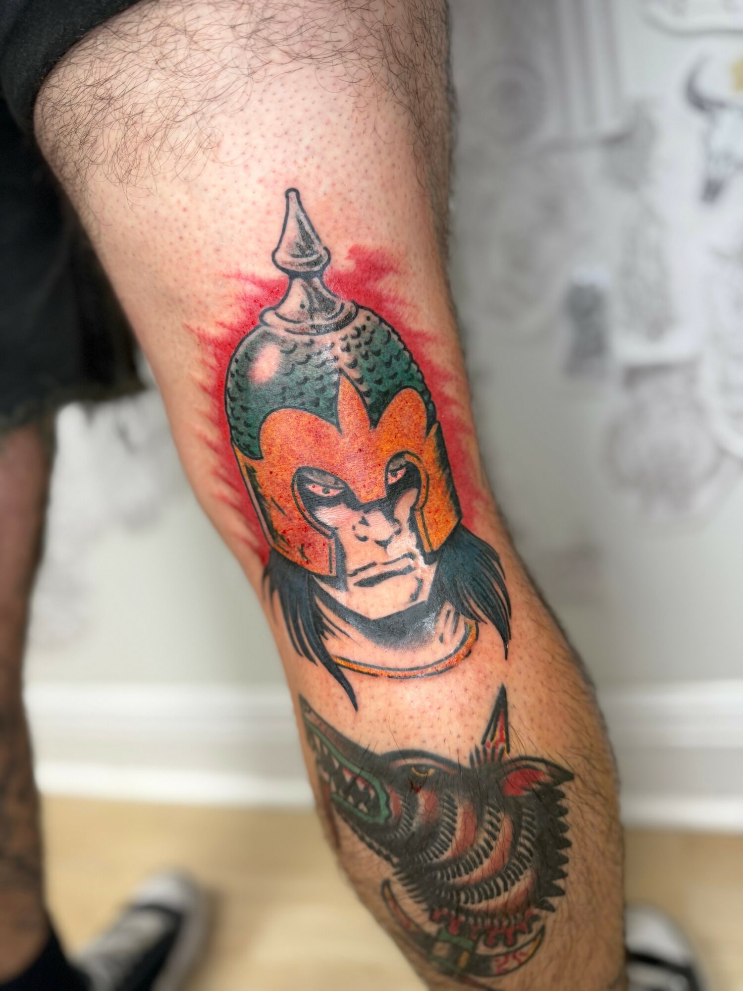 Tattoo of a lion's face with a fiery background on a person's leg, with a detailed fish below.