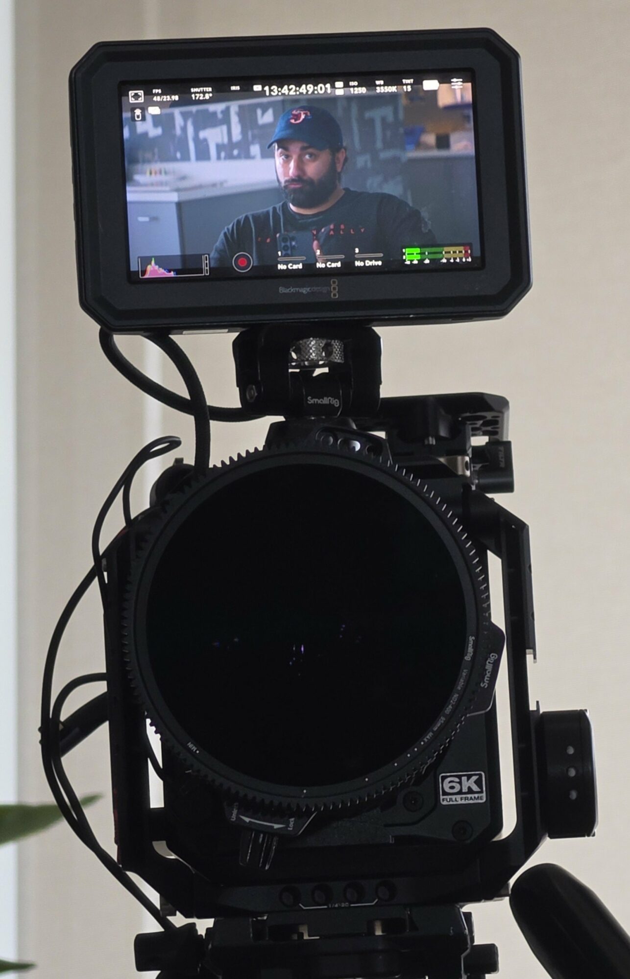 Camera viewfinder showing a man with a beard and glasses, with a cityscape background, on a camera setup.