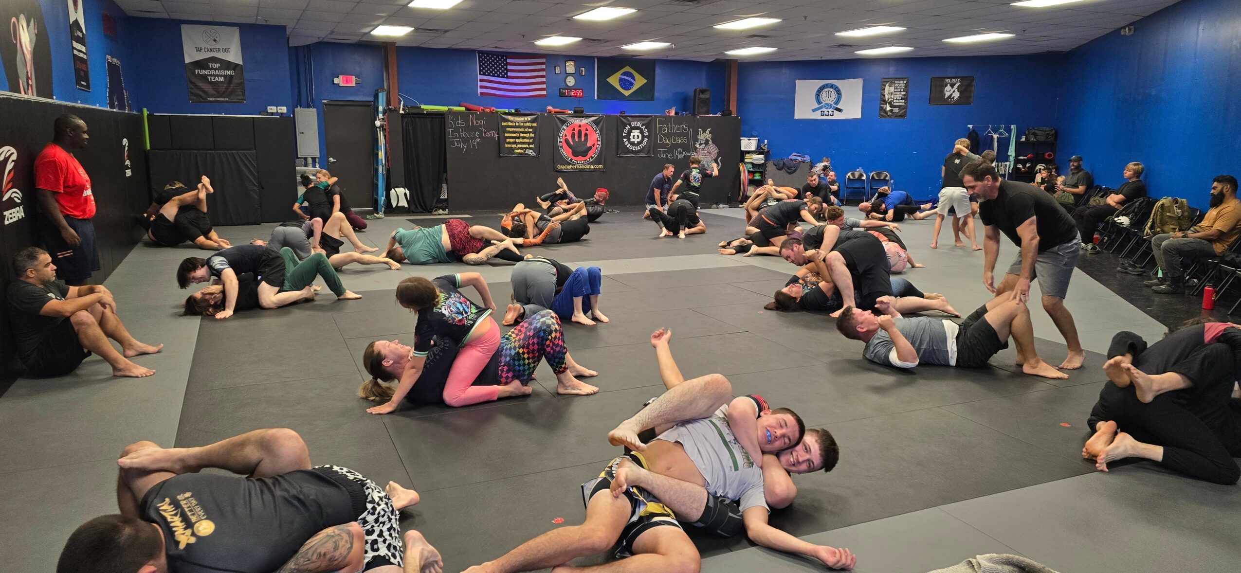 People practicing Brazilian Jiu-Jitsu on mats in a training facility with flags and banners on walls.