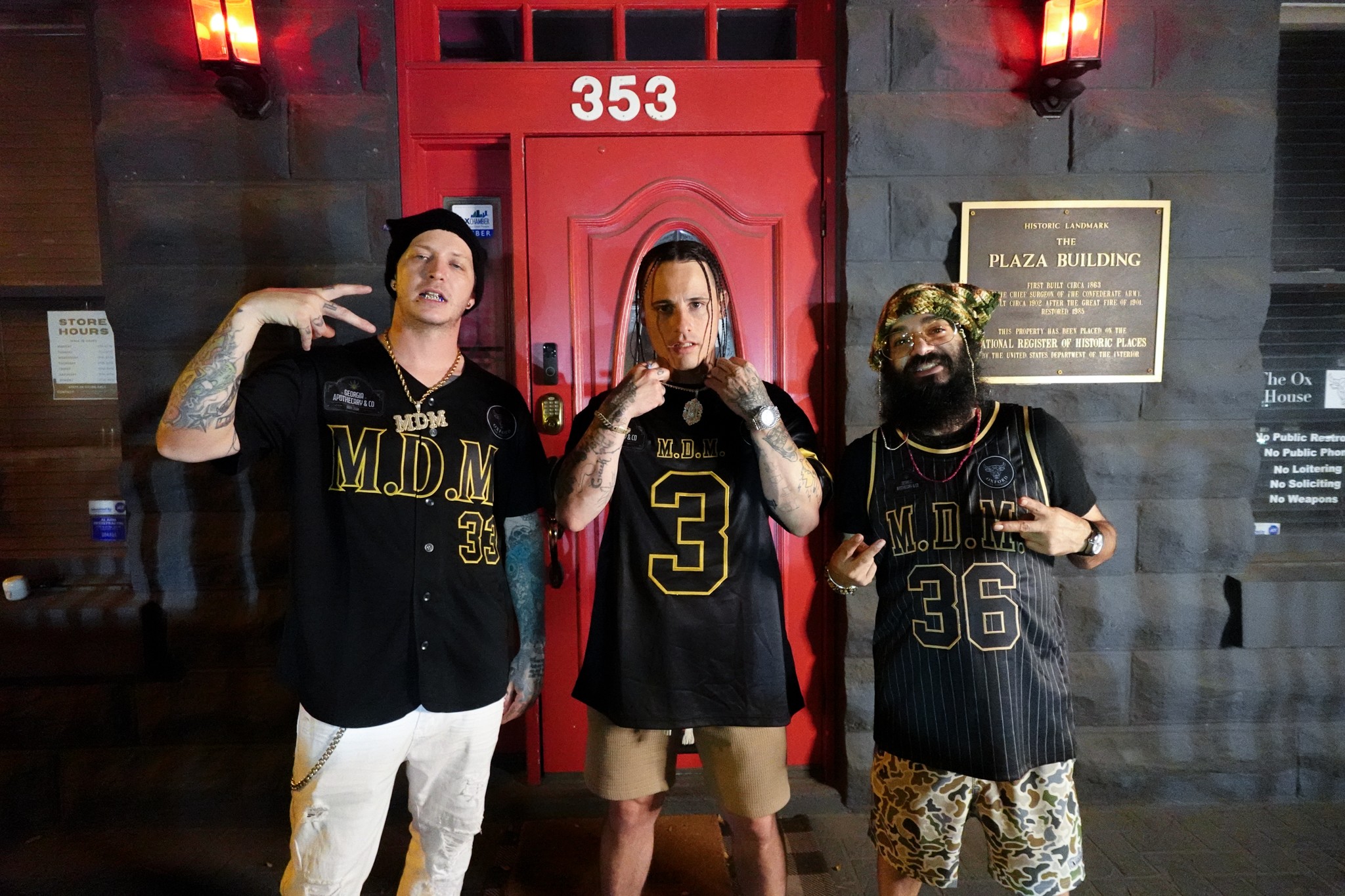 Three people in sports jerseys standing in front of a red door with the number 353, posing with serious expressions.