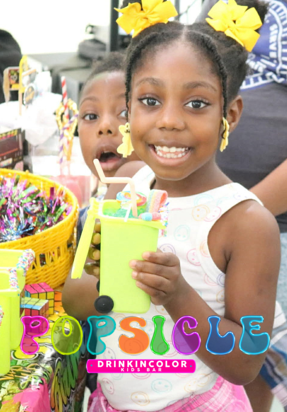 Two smiling young girls with yellow bows in hair, holding colorful items, surrounded by baskets and decorations, at a celebration.