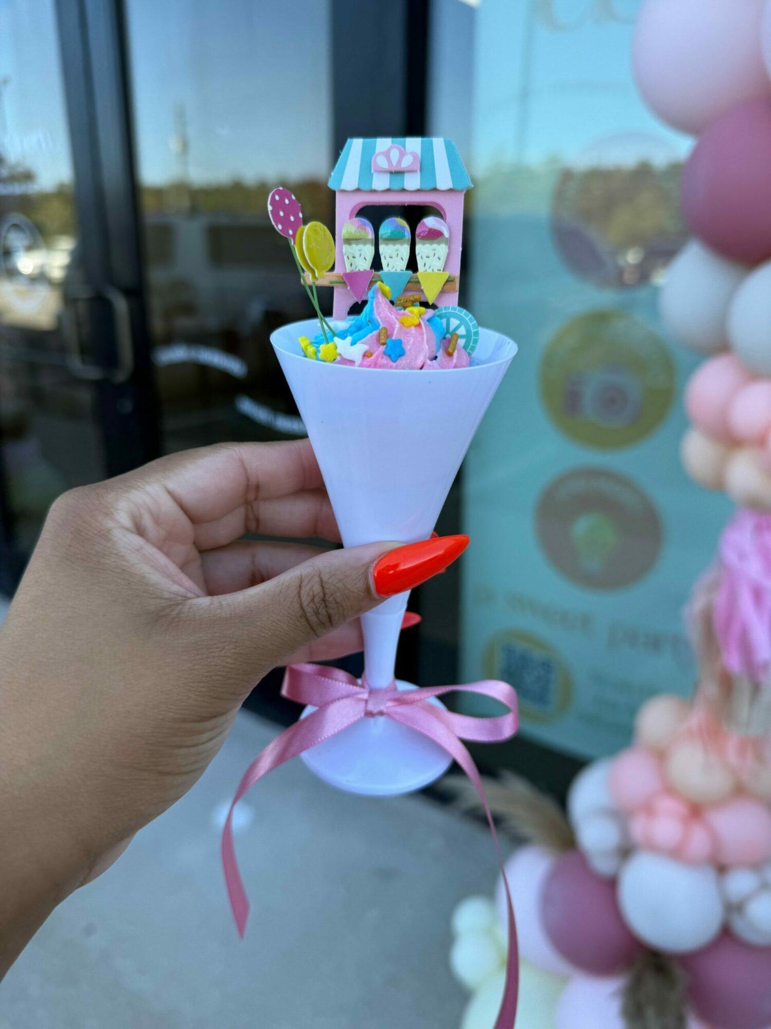 Hand holding a colorful paper craft with a pink ribbon bow, against a background of pastel decorations.