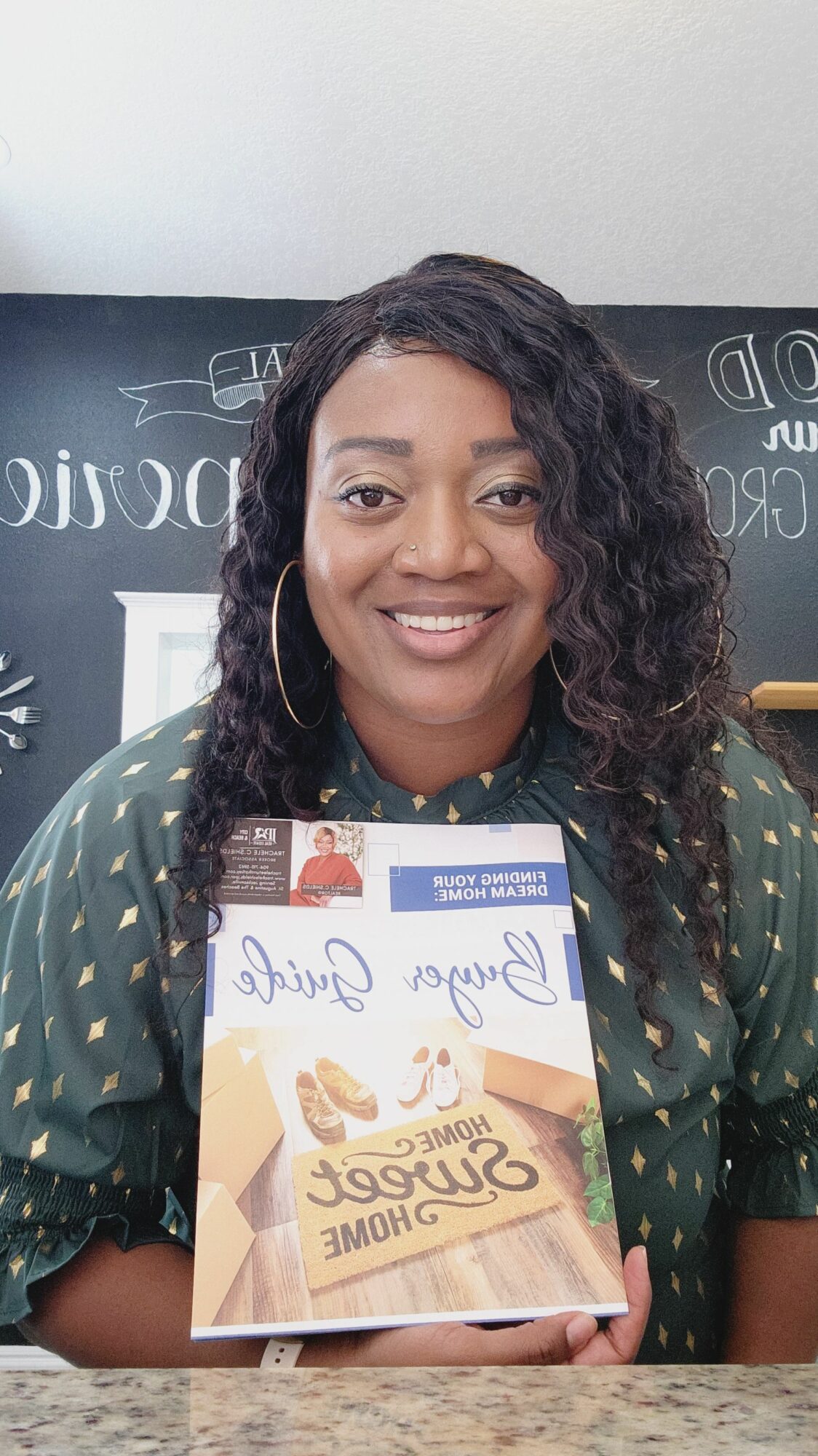 Woman with curly hair holding a chocolate bar, smiling, in front of a chalkboard with writing.