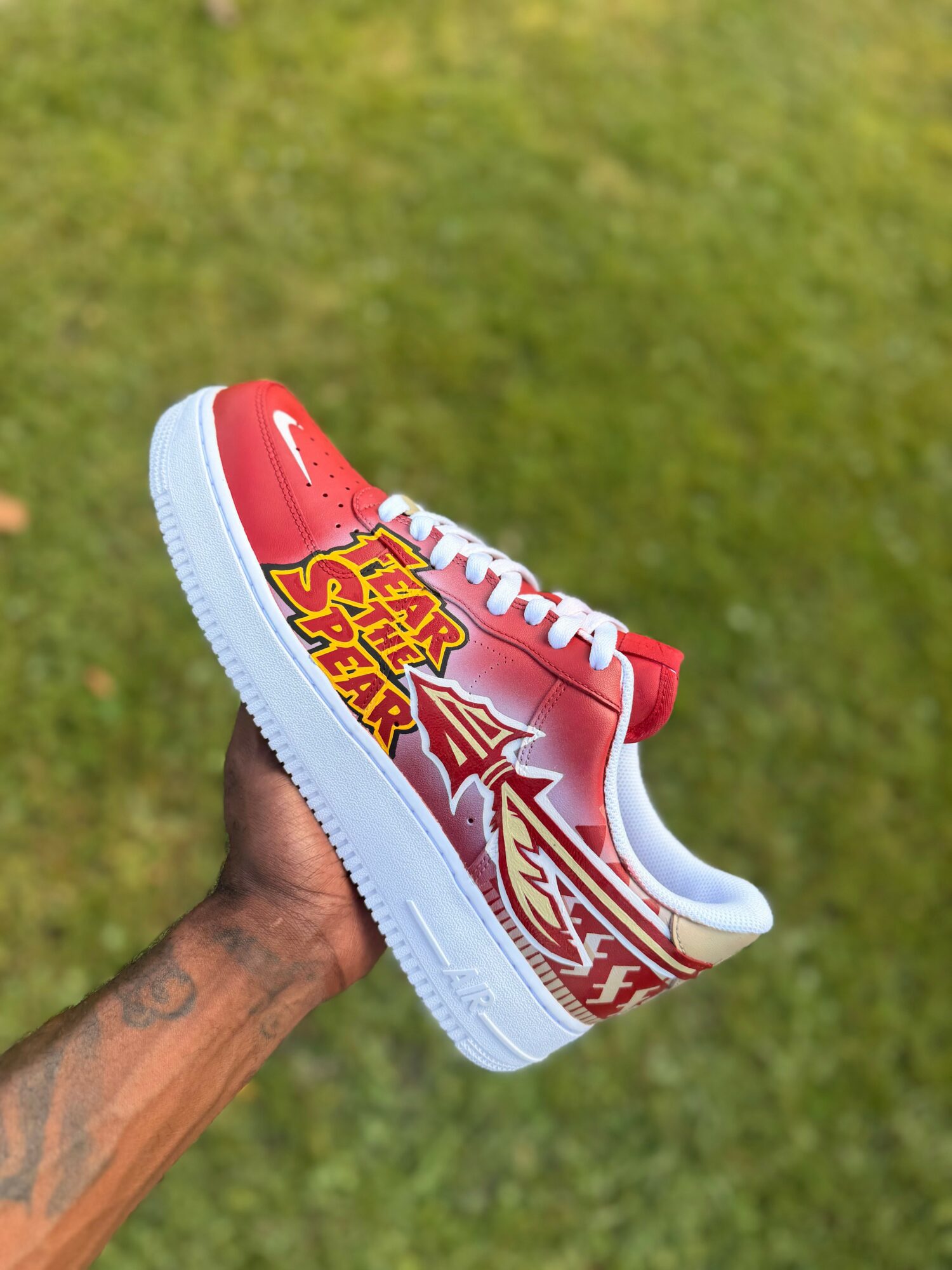 Person holding a red and white sneaker with a grassy background.