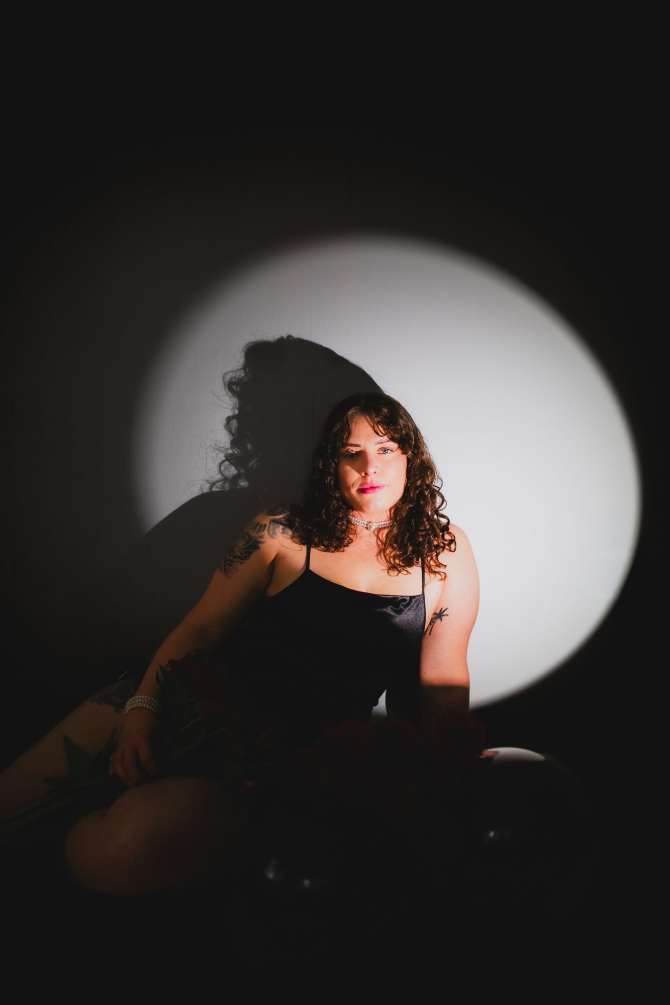 Woman with curly hair sitting in front of a spotlight, casting a shadow on the wall behind her.
