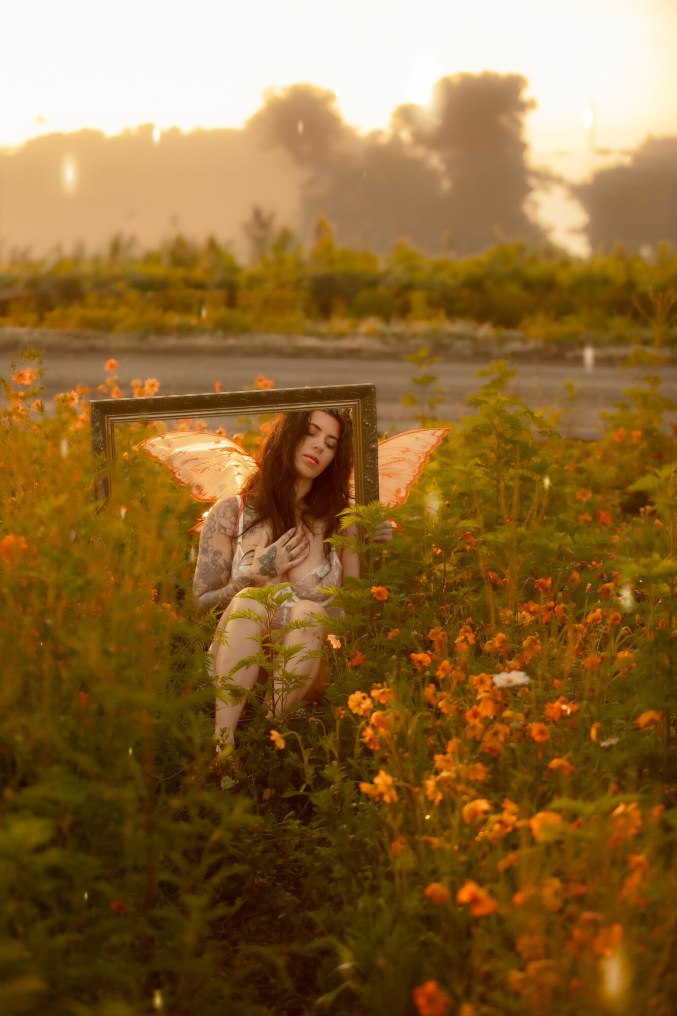 Woman sitting in a field of orange flowers with a picture frame around her, sunset sky in the background.