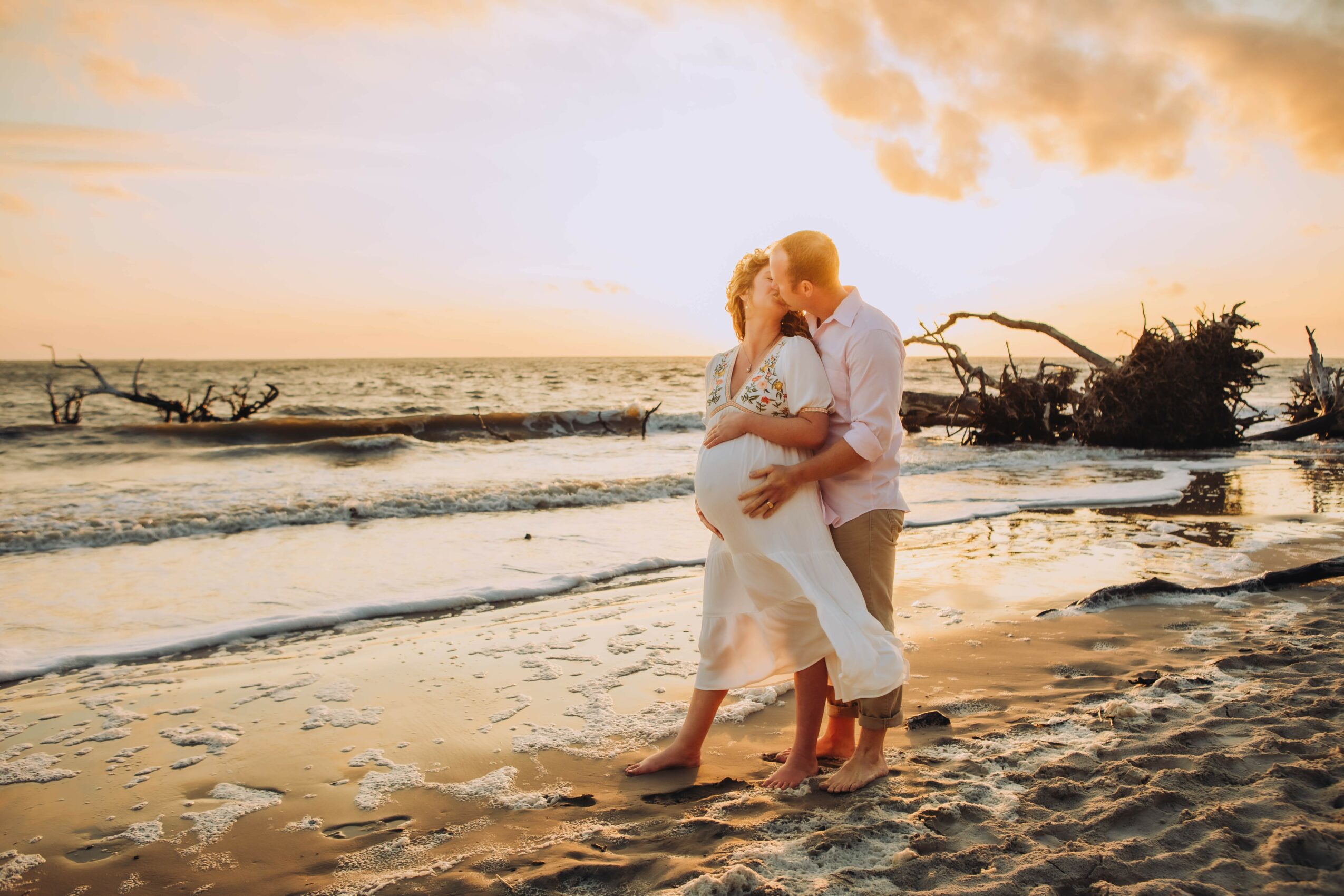 A couple dancing on a beach at sunset, with waves and driftwood in the background.