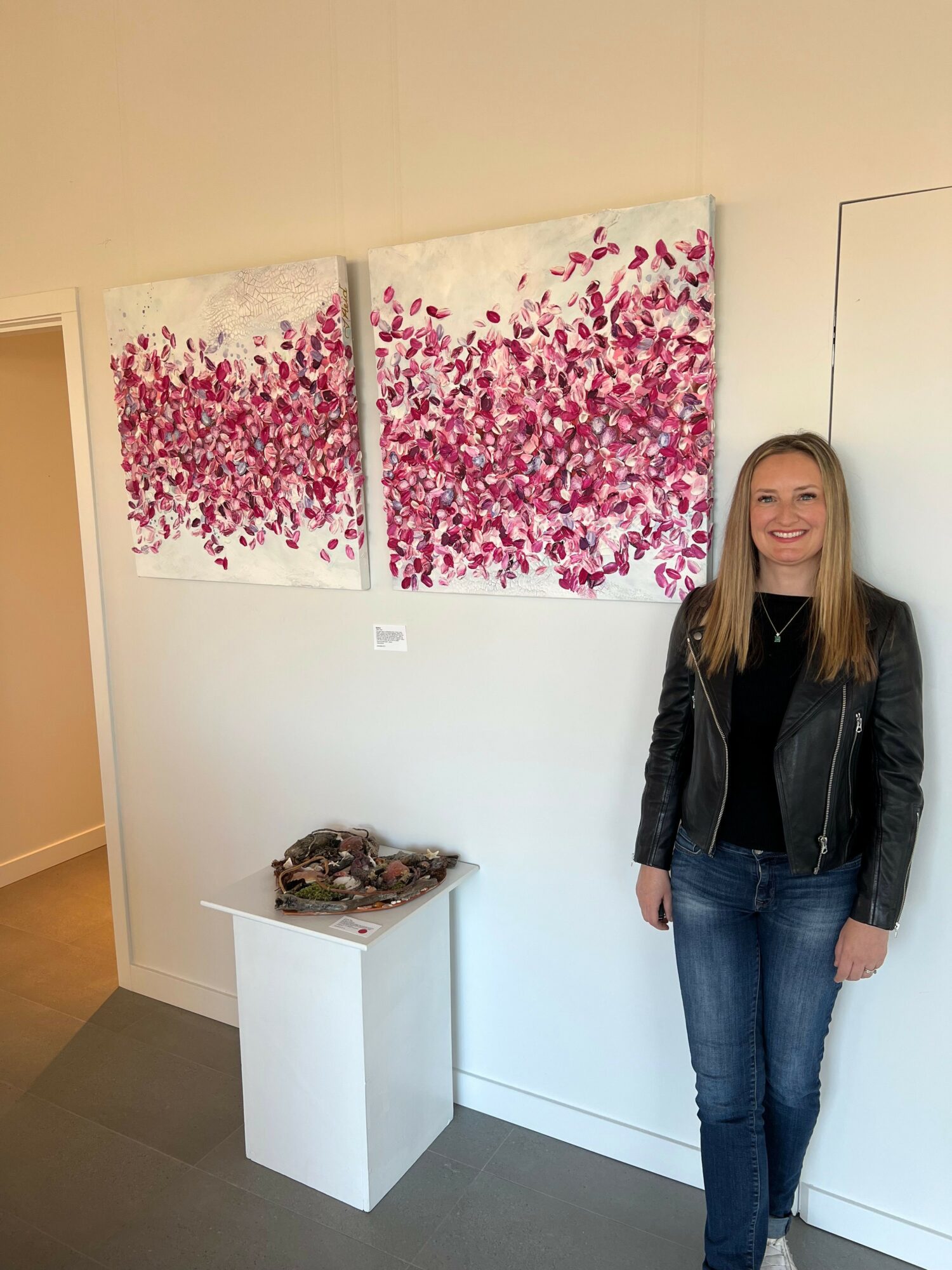 Woman standing next to two abstract pink and red paintings on a white wall, with a white pedestal below.
