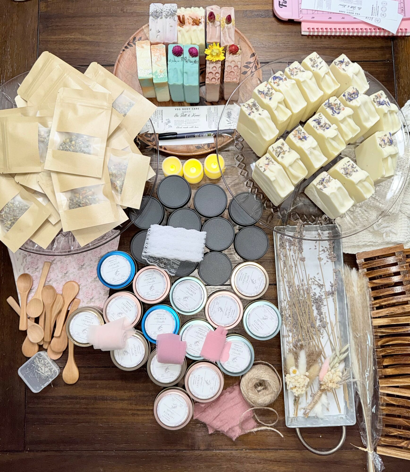 Assorted soap bars, small jars, wooden spoons, and a soap dish on a wooden table.