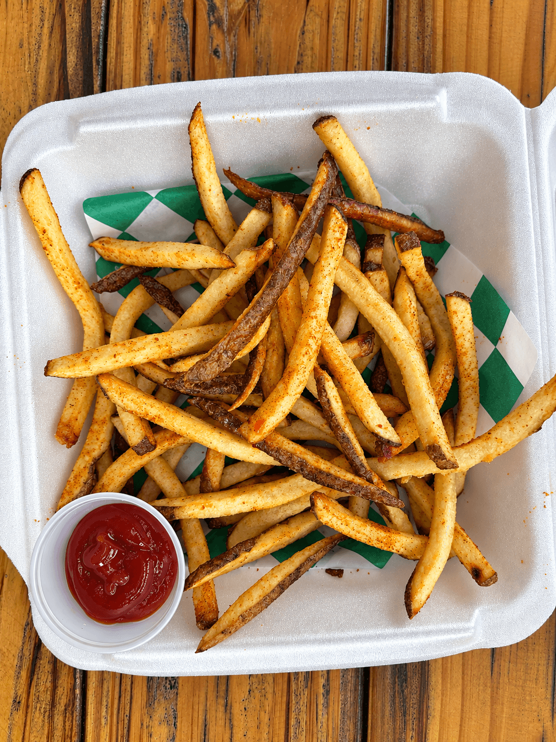 French fries with a small cup of ketchup on a white tray, placed on a wooden surface.