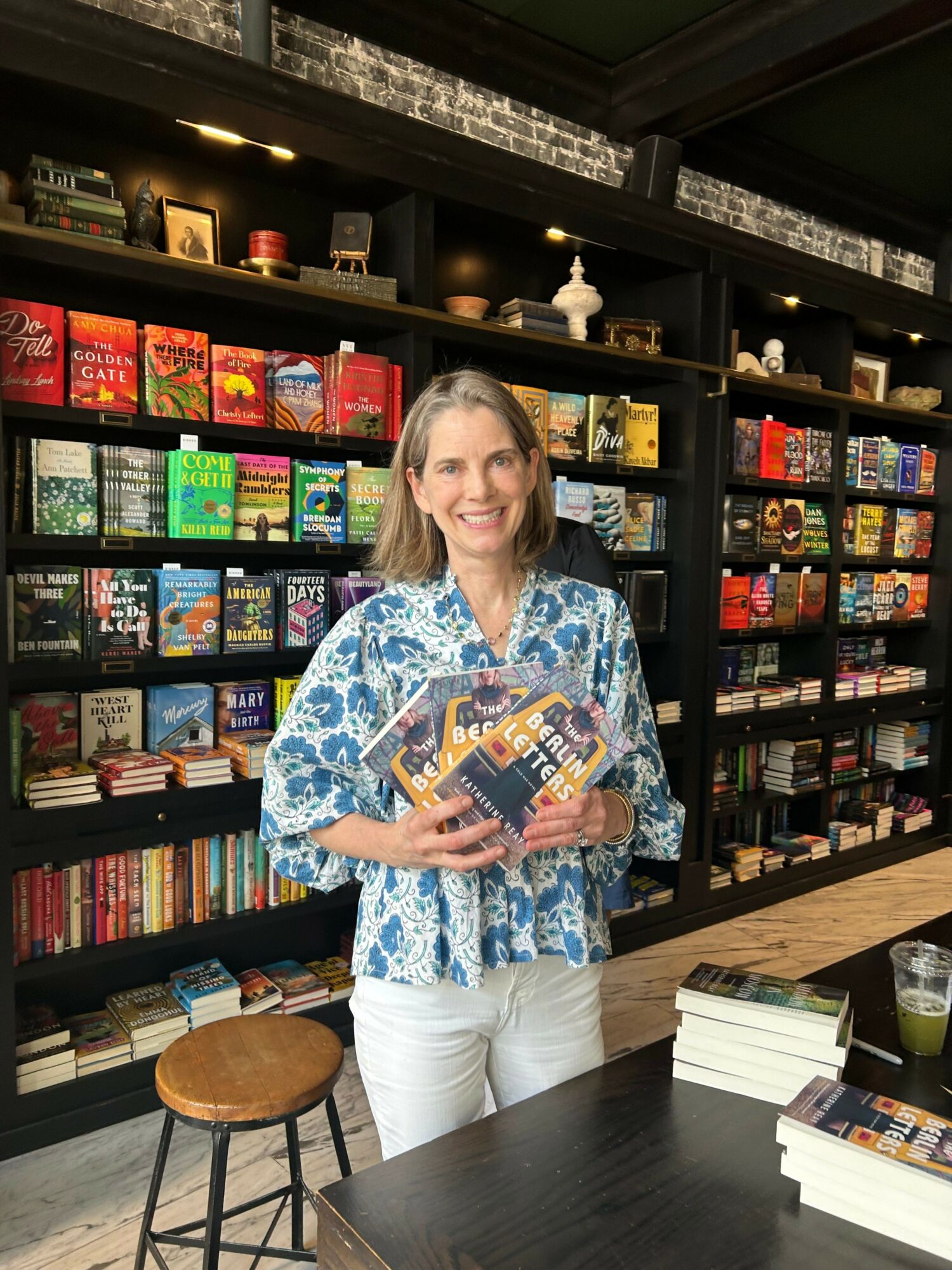 Woman holding a colorful book in a bookstore with shelves of books behind her.