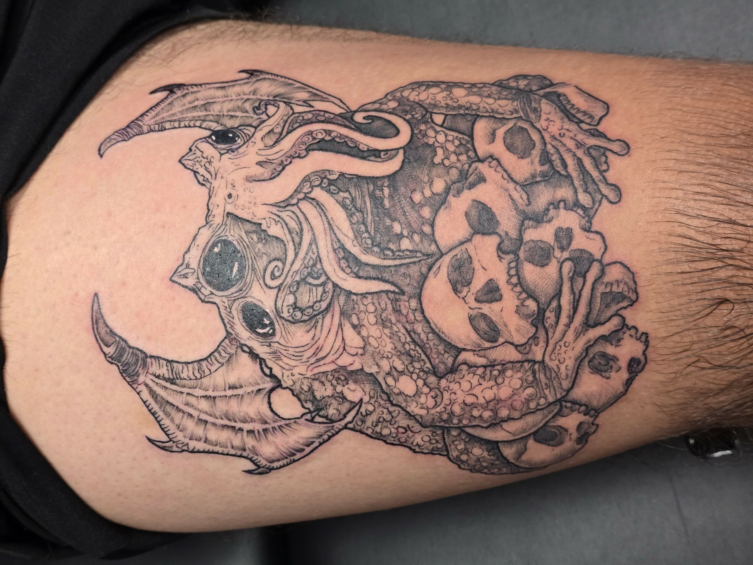 Detailed tattoo of a dragon and a creature with multiple eyes and tentacles on a person's arm.