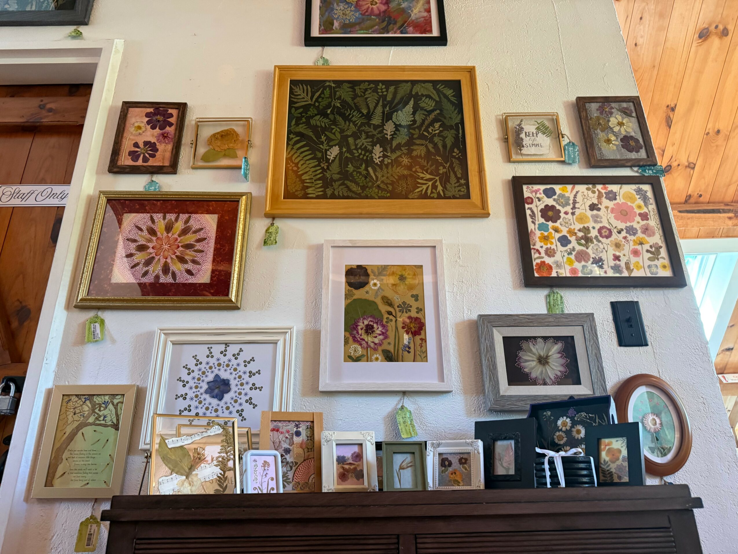 Wall decorated with framed artwork and photographs, including a large central piece with green foliage, and smaller colorful images.