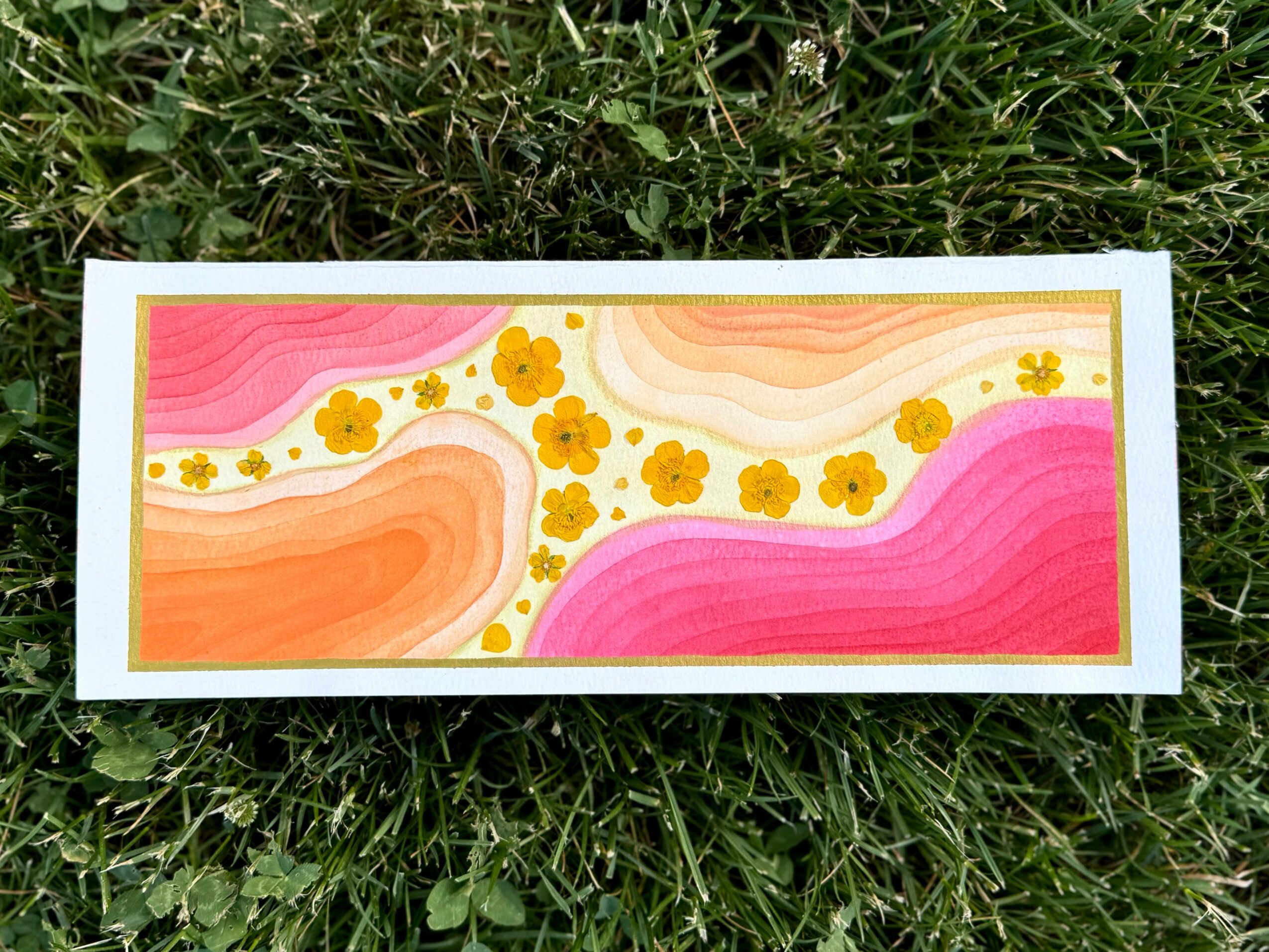 Colorful abstract painting with pink, orange, and yellow swirls and yellow flowers on a white background, on grass.