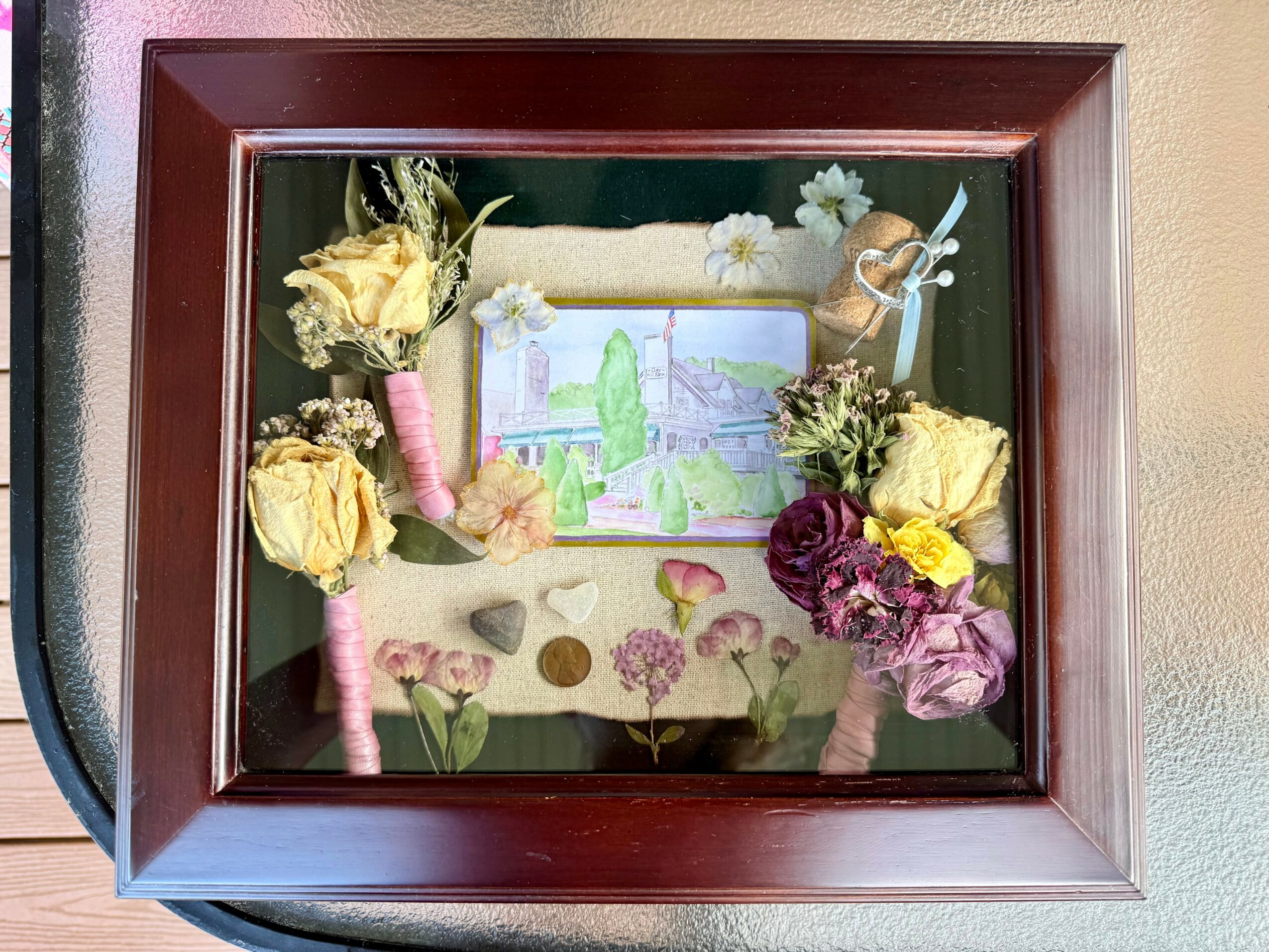 Framed shadow box with dried flowers, a small drawing, and decorative elements inside.