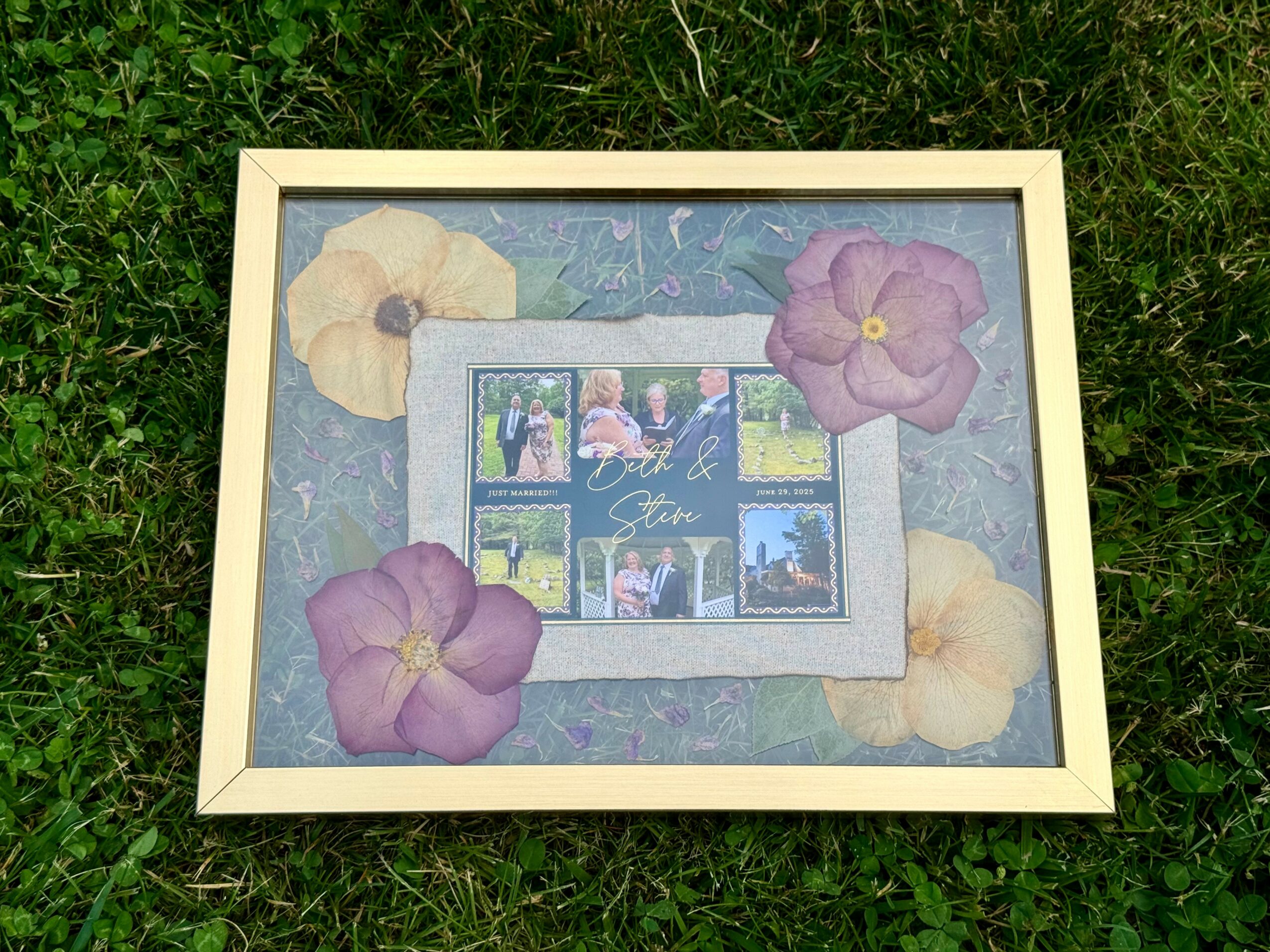 Framed collage of photos with purple and cream paper flowers on a grassy surface.