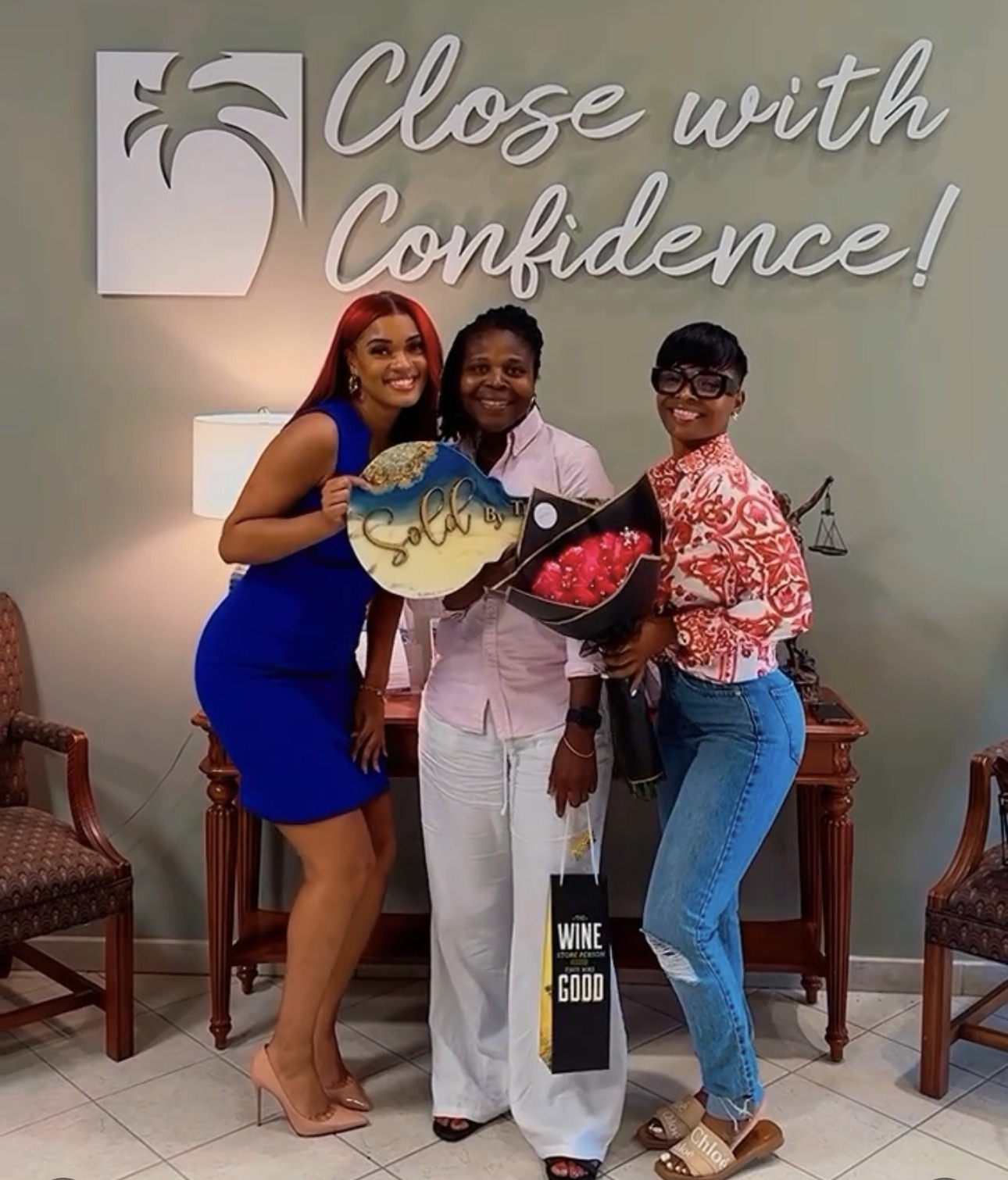 Three women standing together in front of a wall with a sign that says 'Close with Confidence!'.