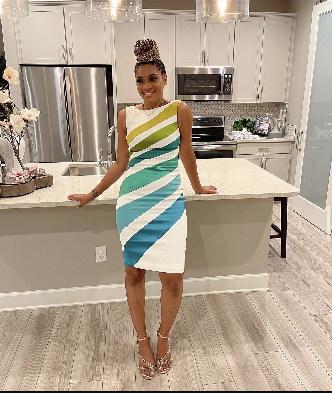 Woman in a colorful striped dress standing in a modern kitchen with white cabinets and stainless steel appliances.