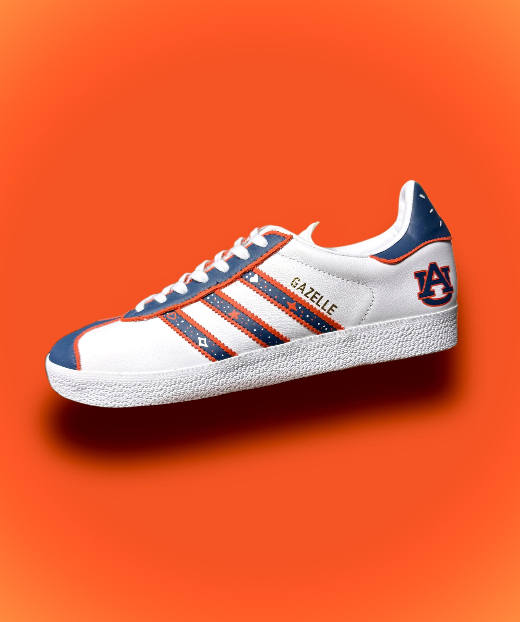 White sneaker with blue and orange accents, featuring the Auburn University logo and the word GAZELLE, on an orange background.