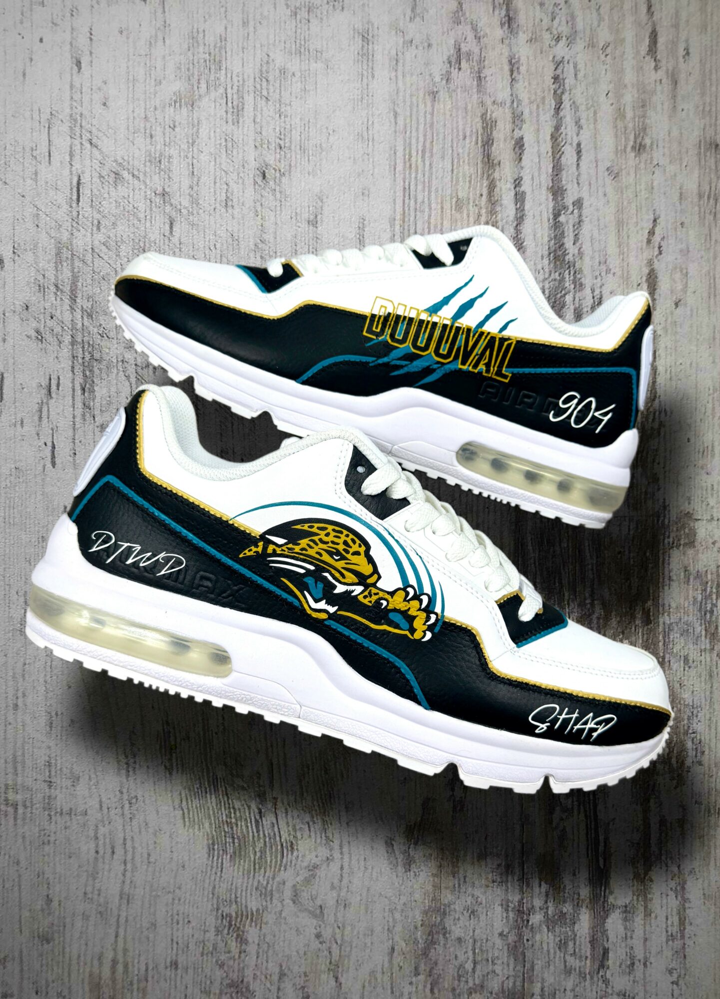Pair of black, white, and blue sneakers with yellow accents on a wooden surface.